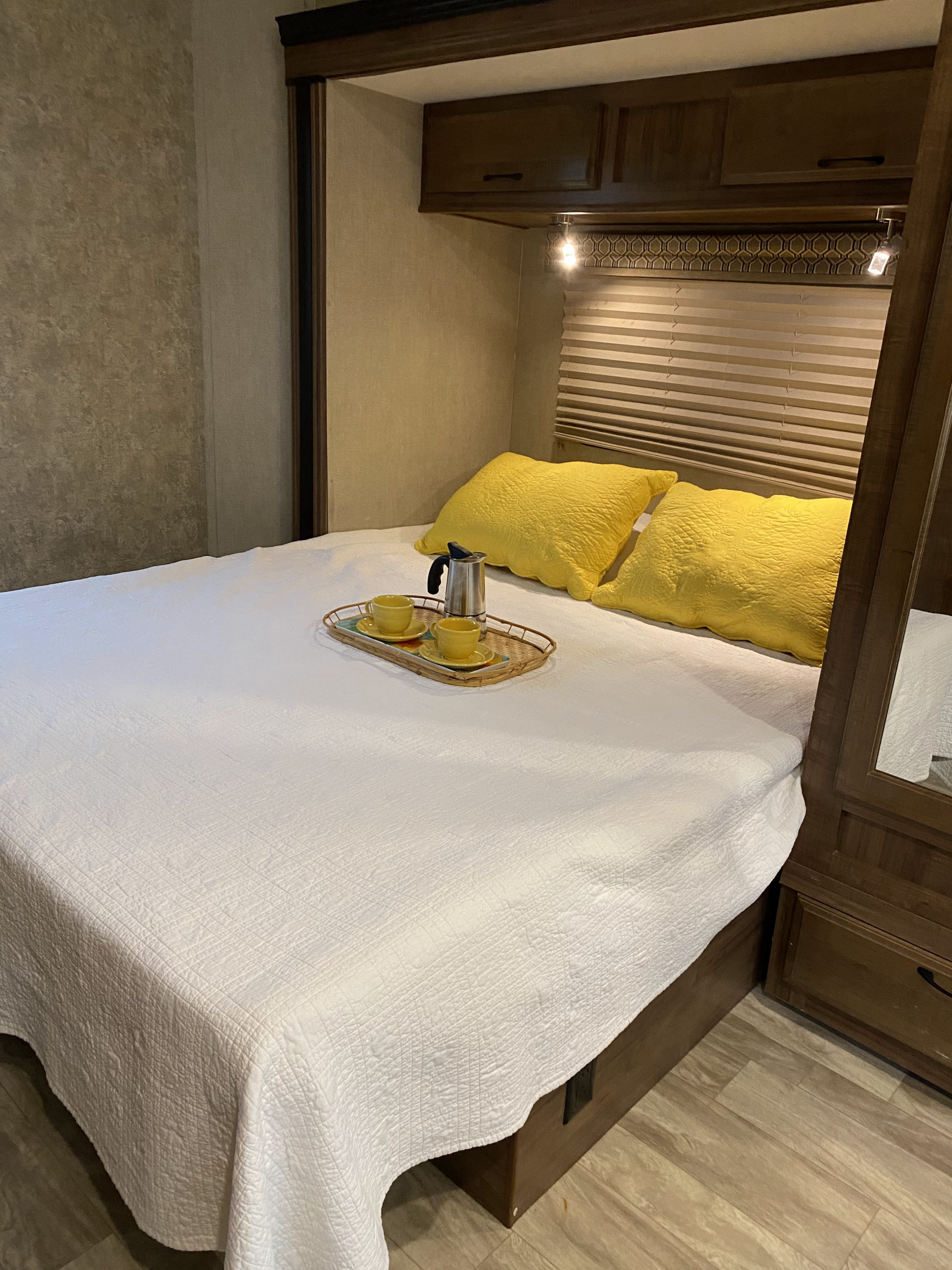 Cozy RV rental bedroom featuring a white bed, bright yellow pillows, and a coffee tray, ideal for comfortable travel.. Gulf Stream Conquest 2019