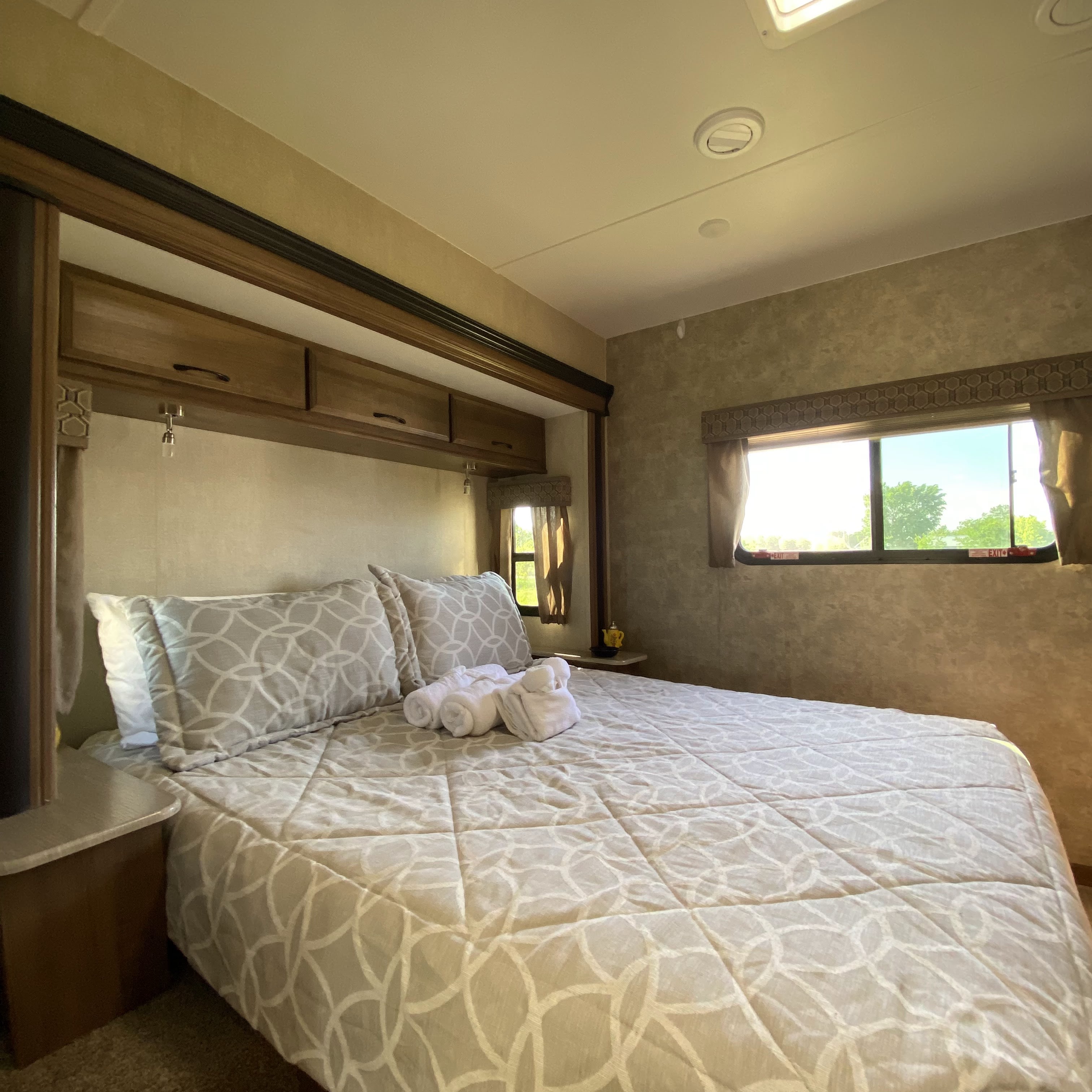 Cozy RV rental bedroom featuring a comfortable bed with patterned bedding, pillows, and convenient overhead storage.. Gulf Stream Conquest 2019