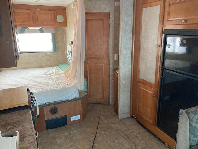 RV rental interior: bed, kitchen counter, refrigerator, curtained bath area, and wood cabinets. A compact living space.. Yellowstone Conquest M6254 2008