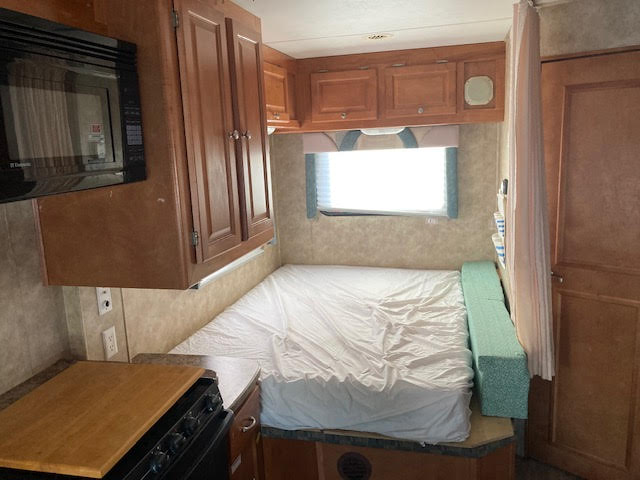 Cozy RV rental interior featuring a bed/dinette area, kitchenette with microwave & stove, and wood cabinets.. Yellowstone Conquest M6254 2008