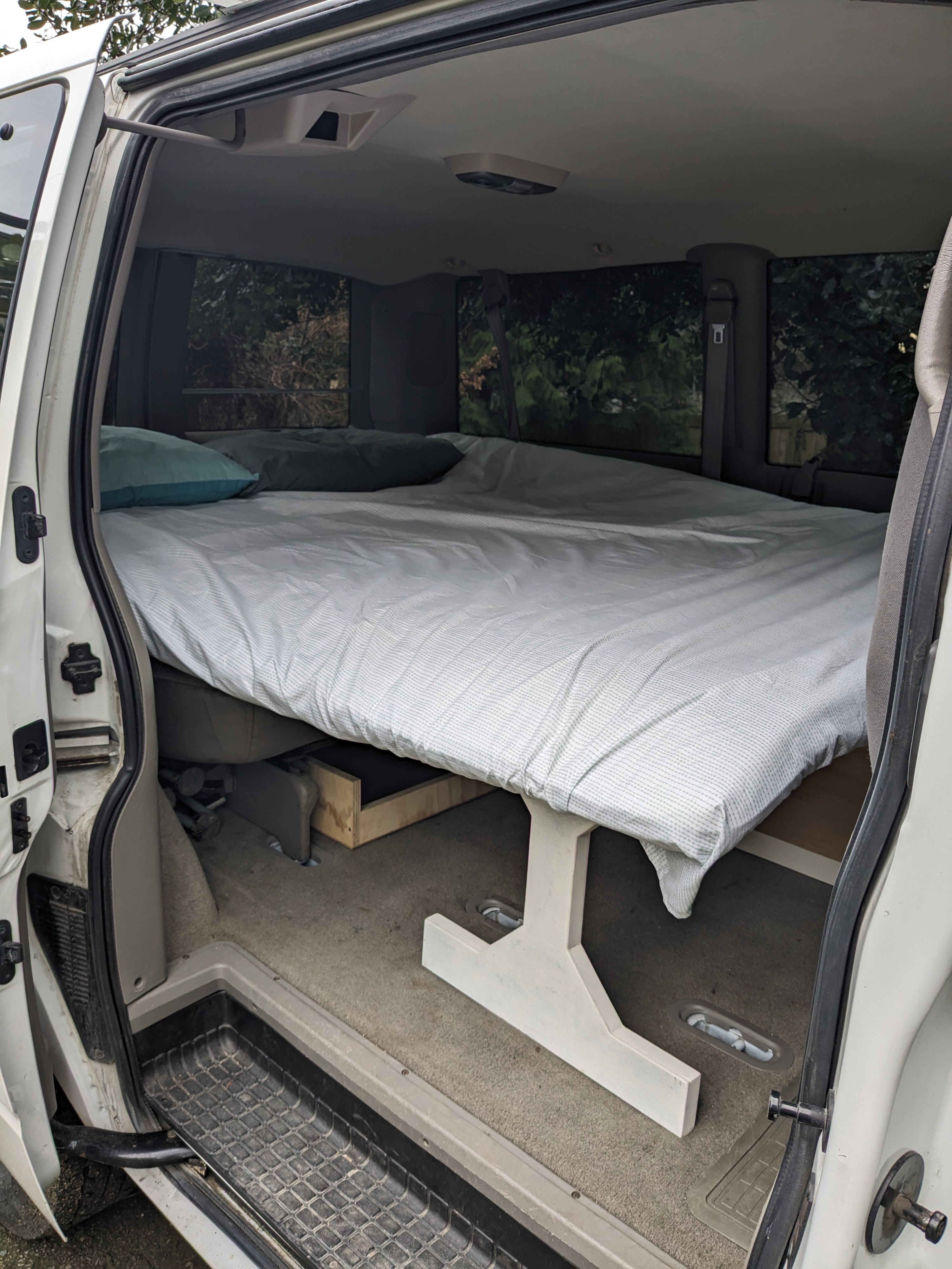 Interior of an RV rental van conversion featuring a large bed with pillows, elevated for storage, ready for camping.. Chevrolet Open Road 2002