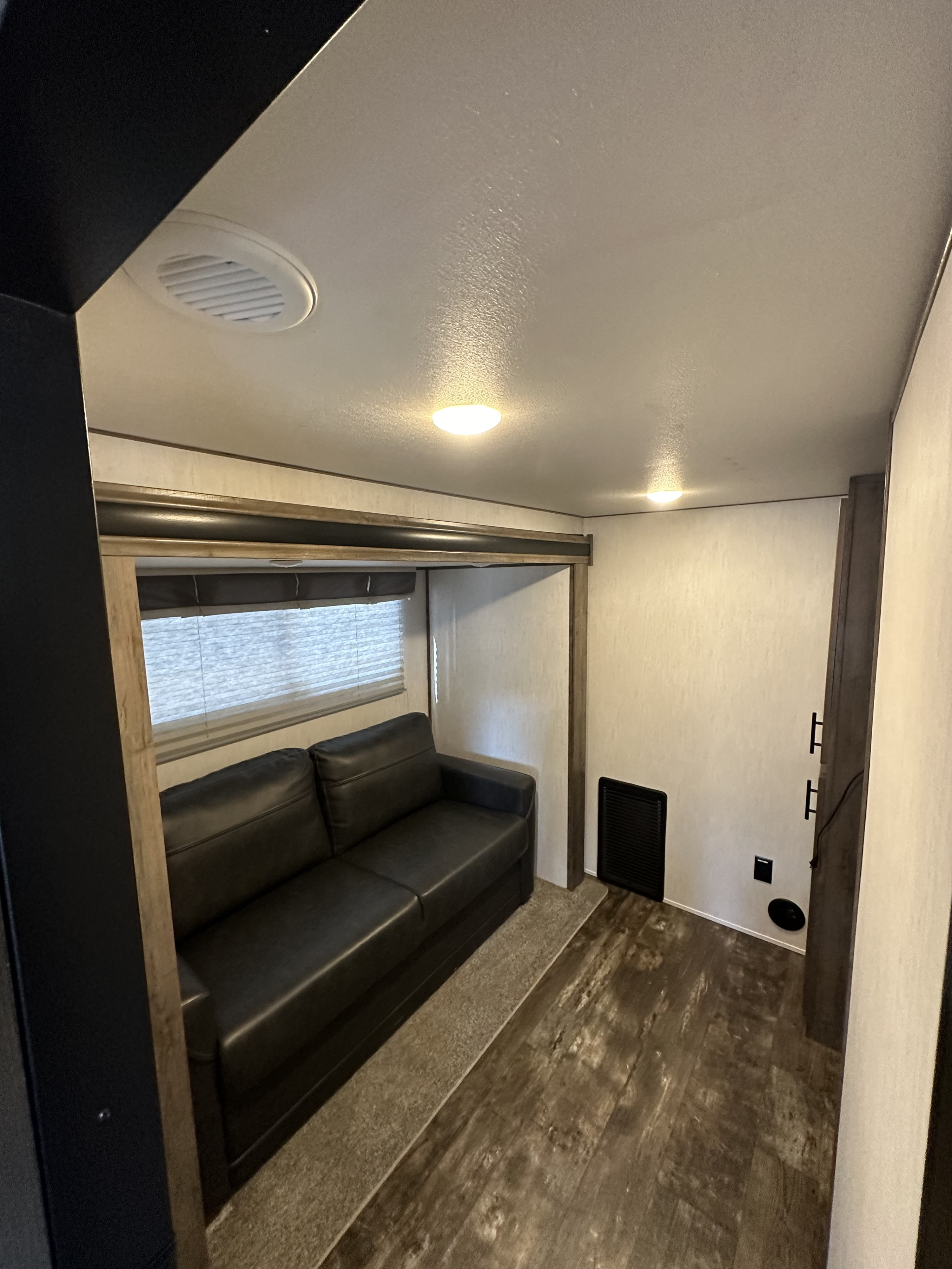 Cozy RV rental interior, showcasing a dark sofa, window with blinds, and wood-look flooring in the living area.. Forest River Sabre 2021