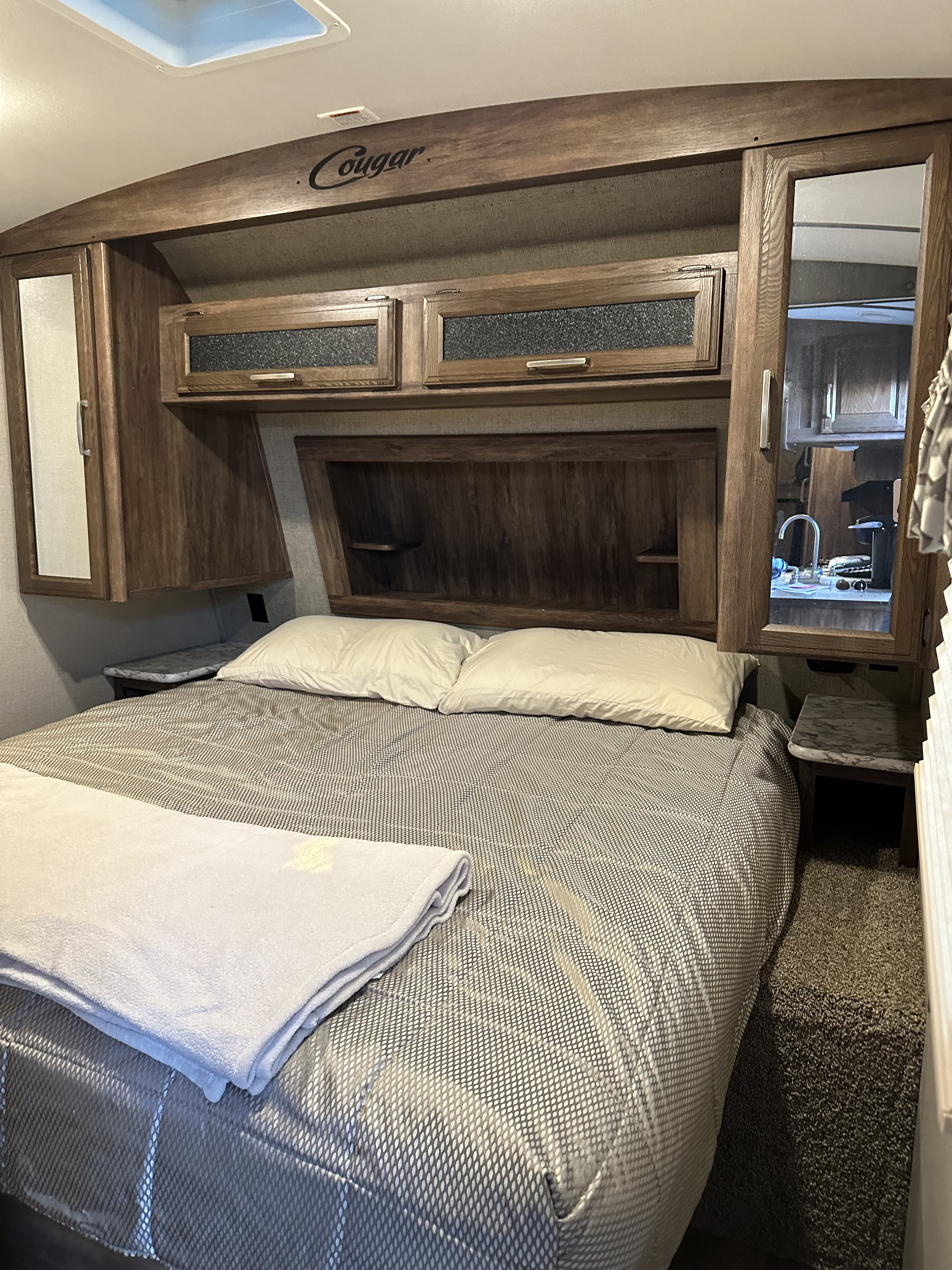 Step into a cozy Cougar RV rental bedroom with a comfortable bed, integrated headboard storage, and sleek overhead cabinets.. Keystone RV Cougar 2019