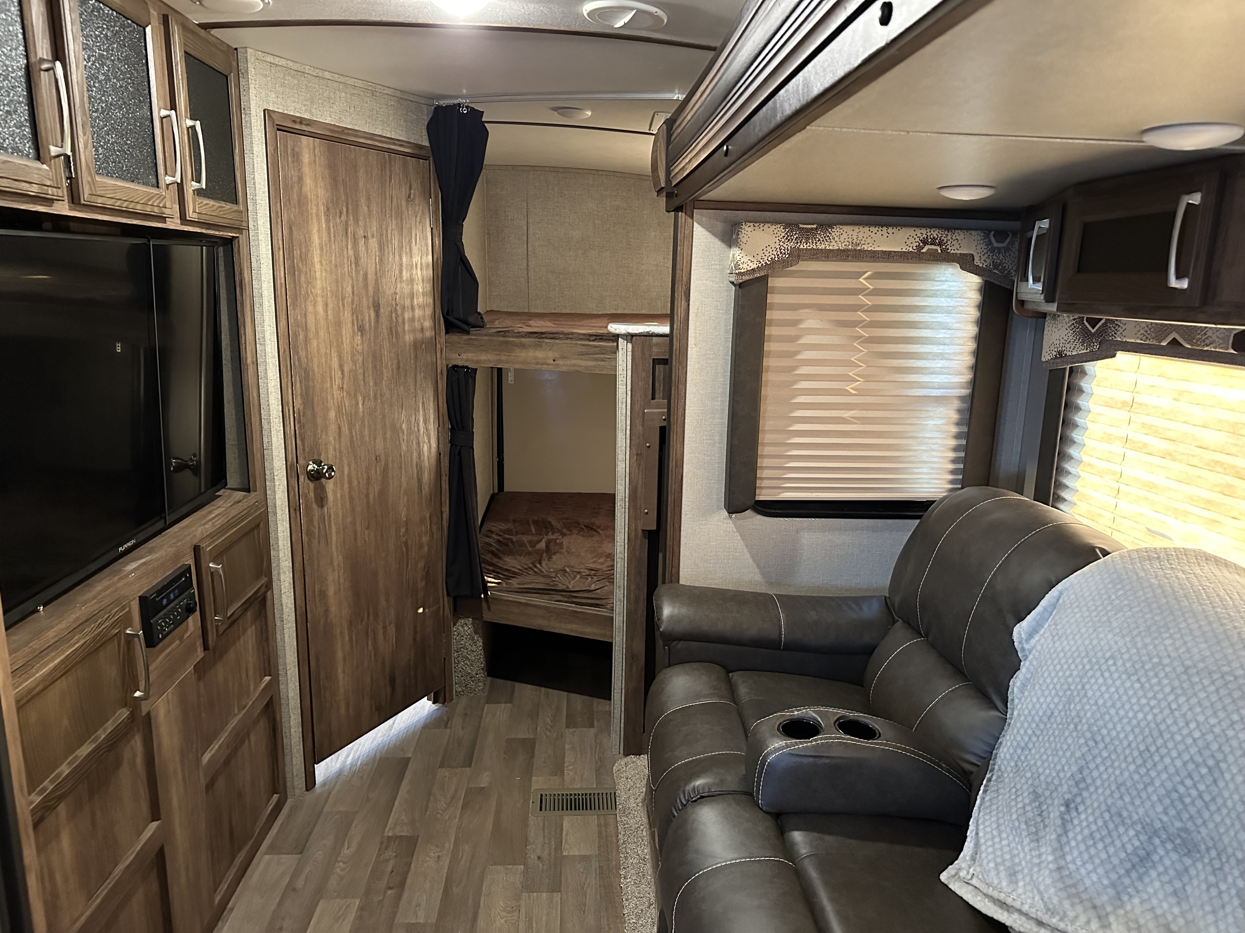 Inside an rv rental: cozy living space with a large TV, plush recliner, and built-in bunk beds.. Keystone RV Cougar 2019