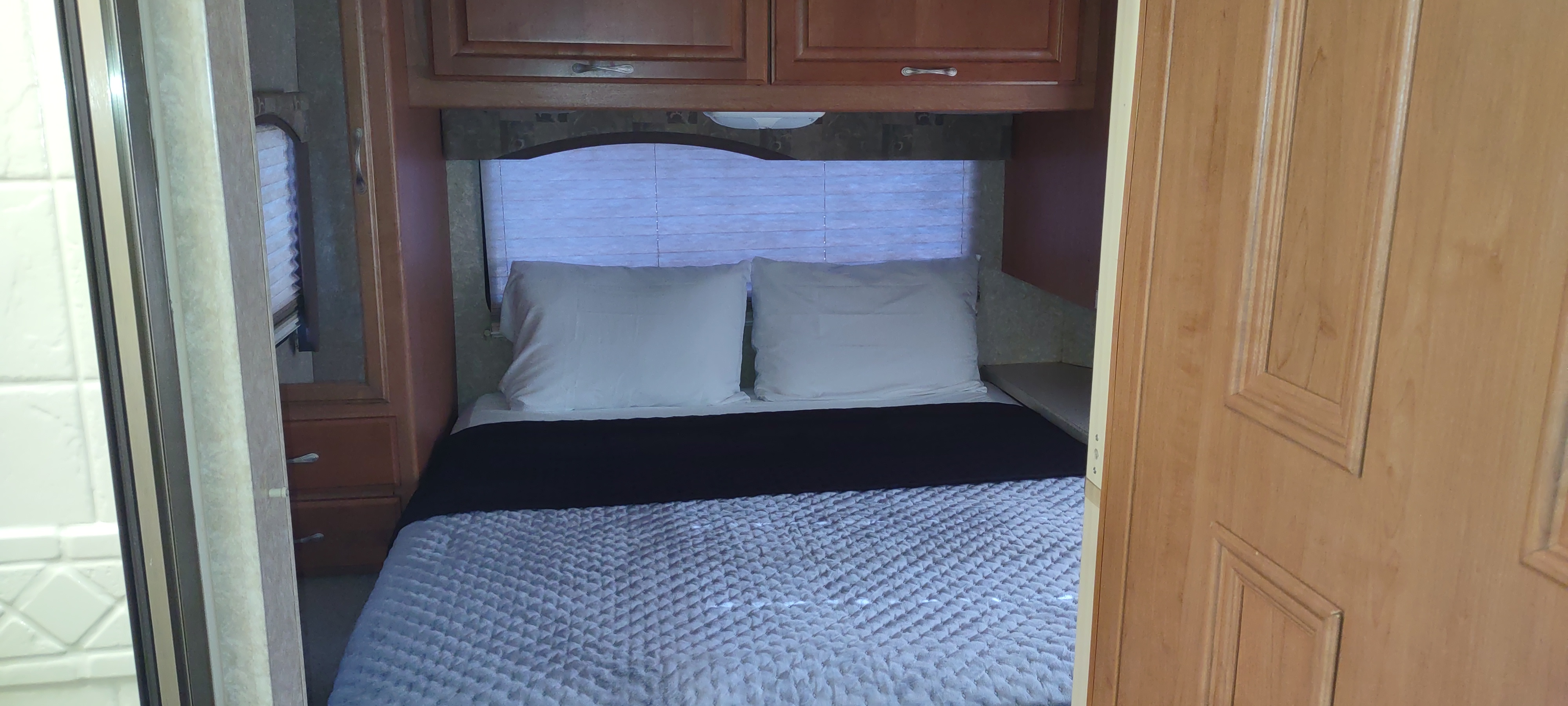 A compact RV rental bedroom with a bed, white pillows, and wooden cabinets. Blinds cover the window. Perfect for an adventure.. Four Winds 5000 2008