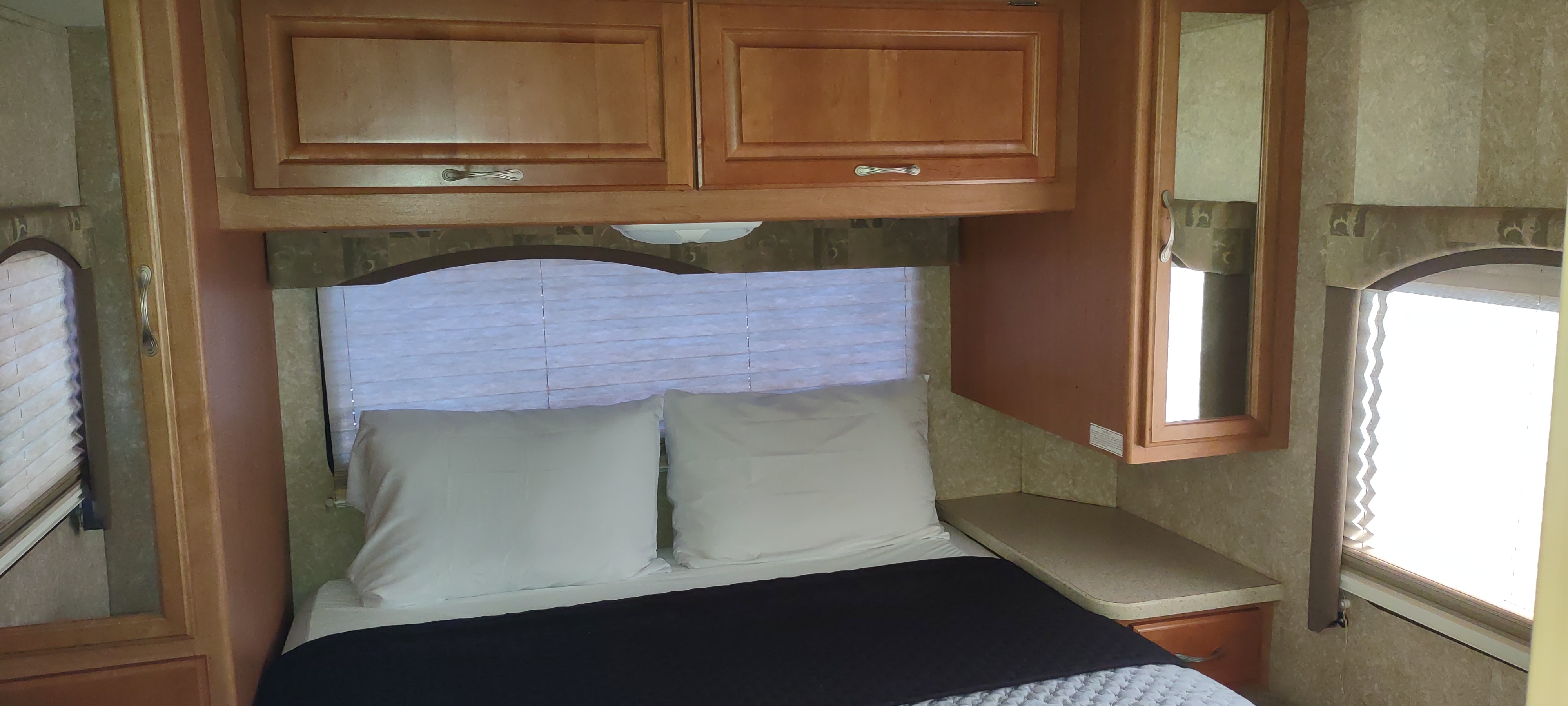 RV rental bedroom: cozy bed with white pillows, overhead cabinets, and windows with blinds.. Four Winds 5000 2008