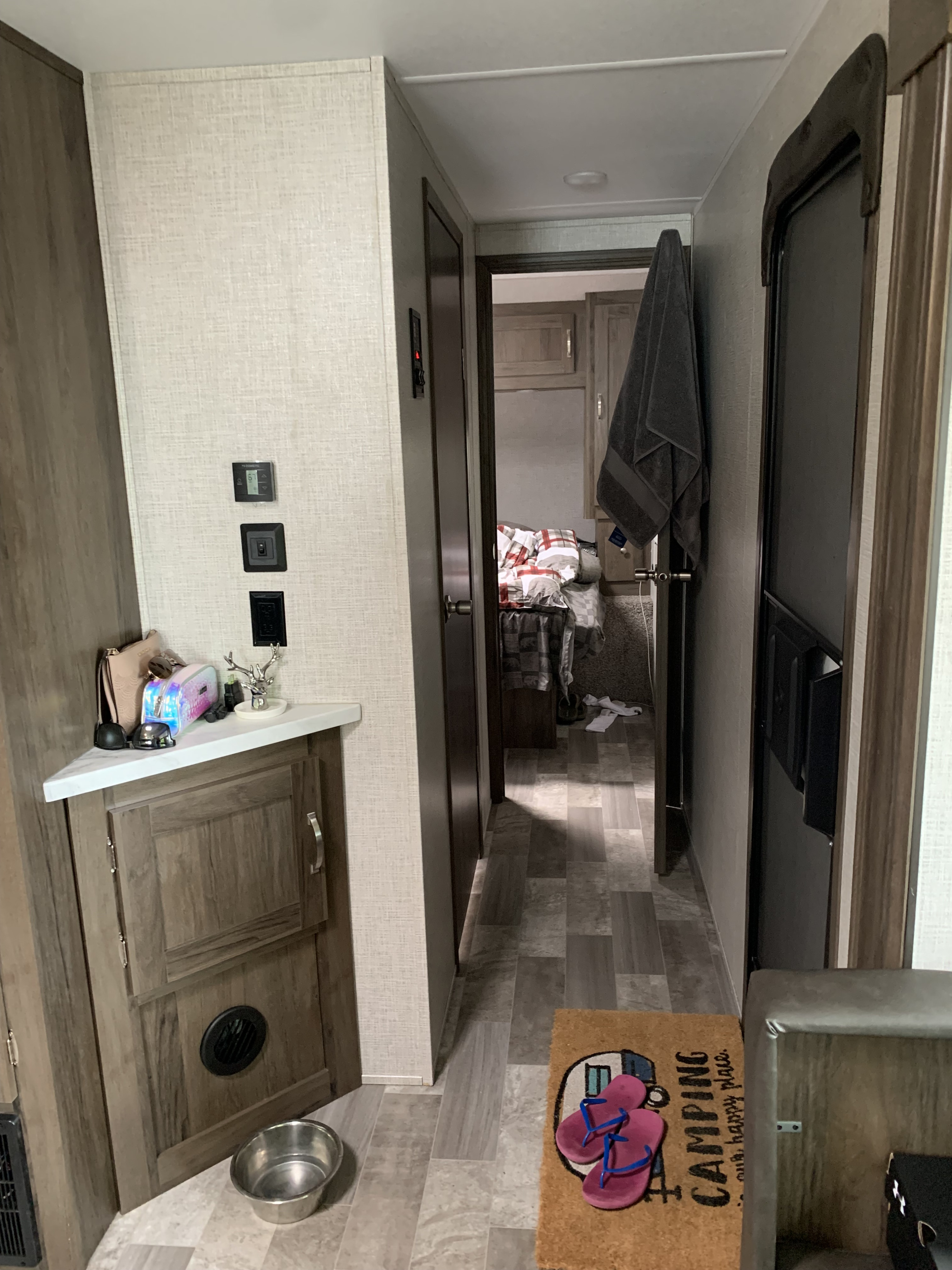Cozy RV rental interior: hallway with personal items, a pet bowl, and a doormat leading to a bedroom.. East to West Della Terra 2021