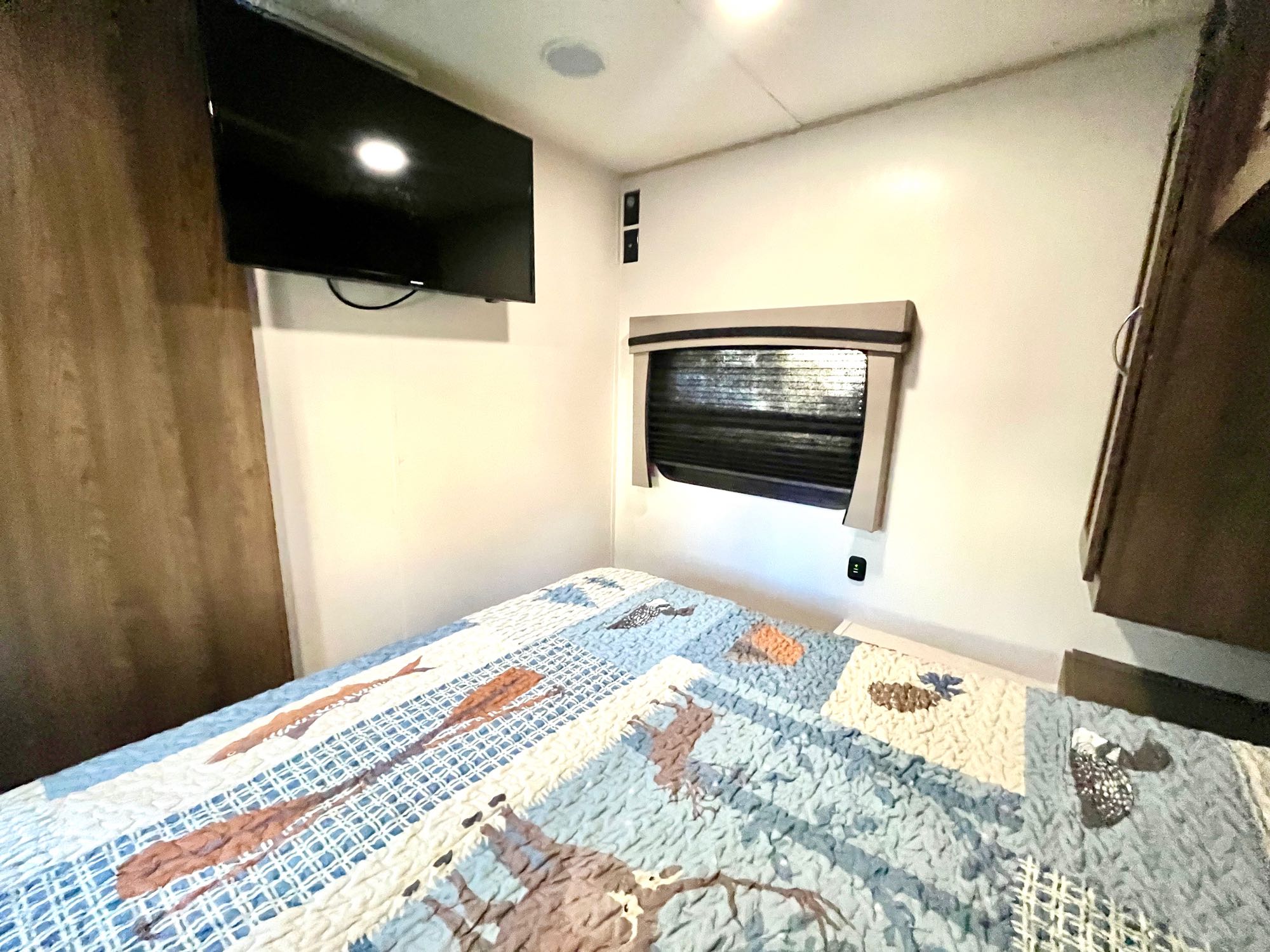 RV rental bedroom with patterned bed, wall-mounted TV, and window, providing a cozy camper interior.. Trail Wagon Chinook Dream D260BH 2021