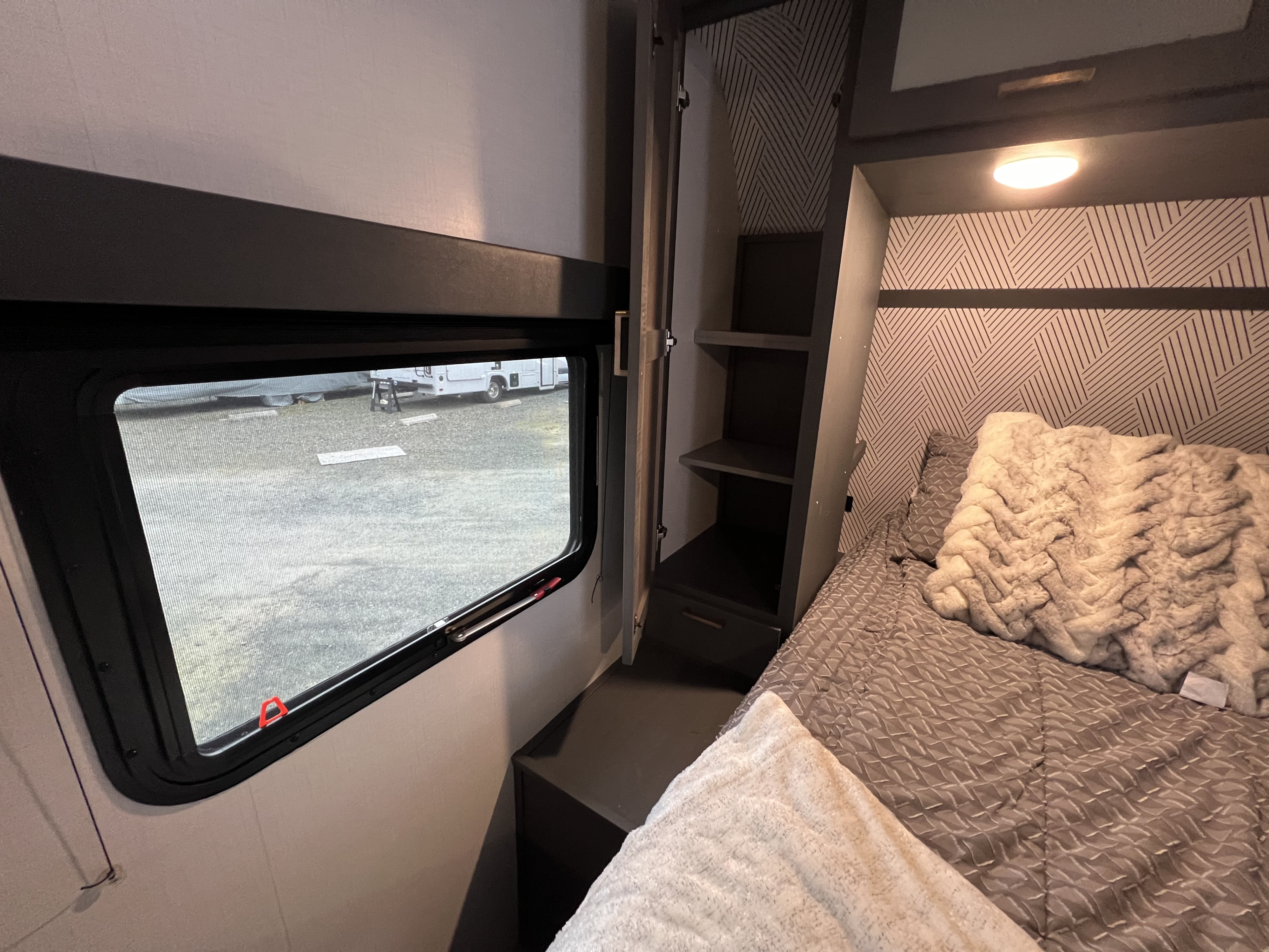 Cozy RV rental bedroom showcasing a window with an outdoor view, a patterned wall, plush bed, and built-in storage.. Keystone RV Bullet Ultra Lite 2022