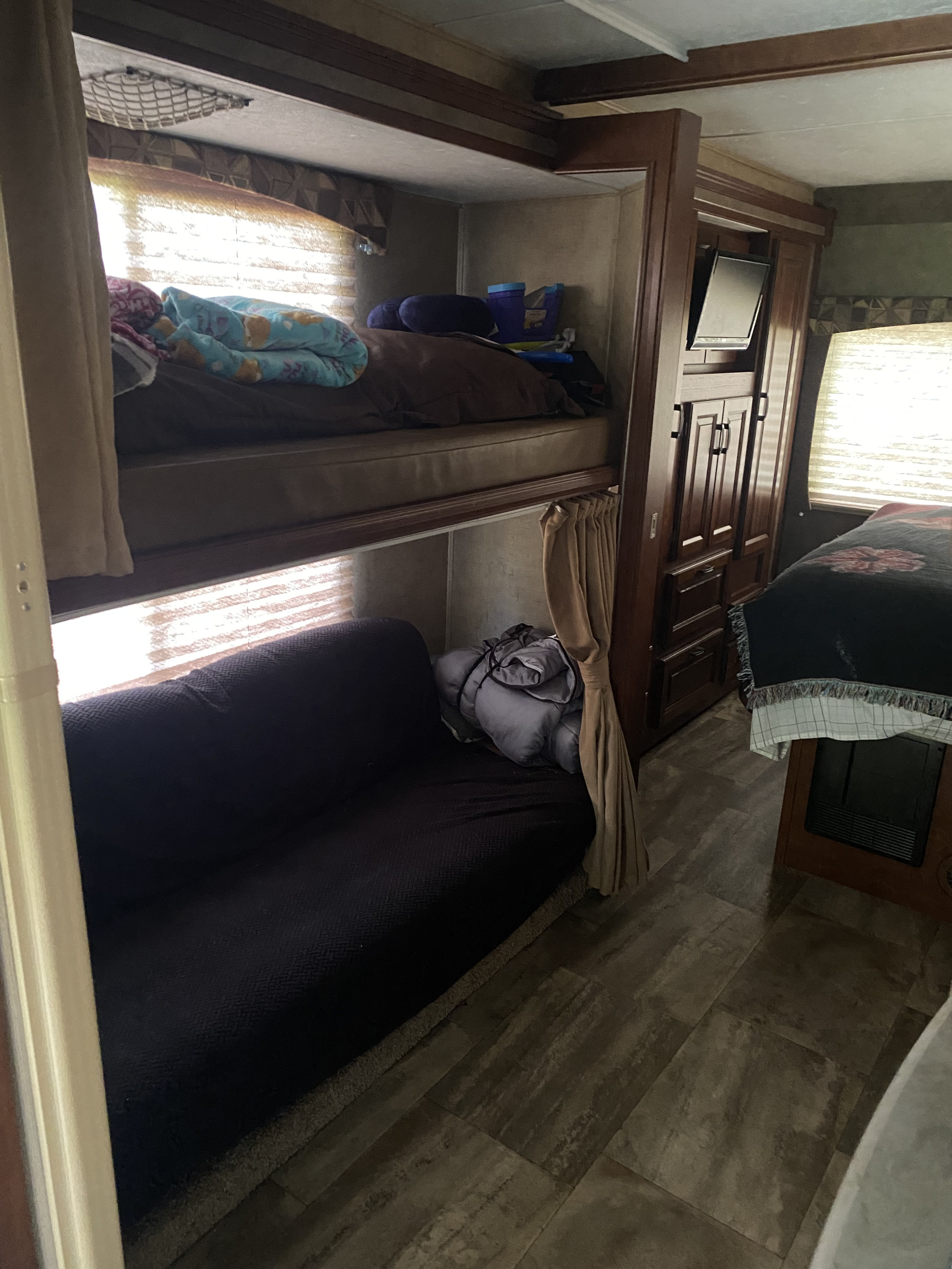 Cozy RV rental interior: bunk beds with a blue blanket, a dark sofa, wooden storage, and a partial view of the main bed.. Forest River Sunseeker 2016