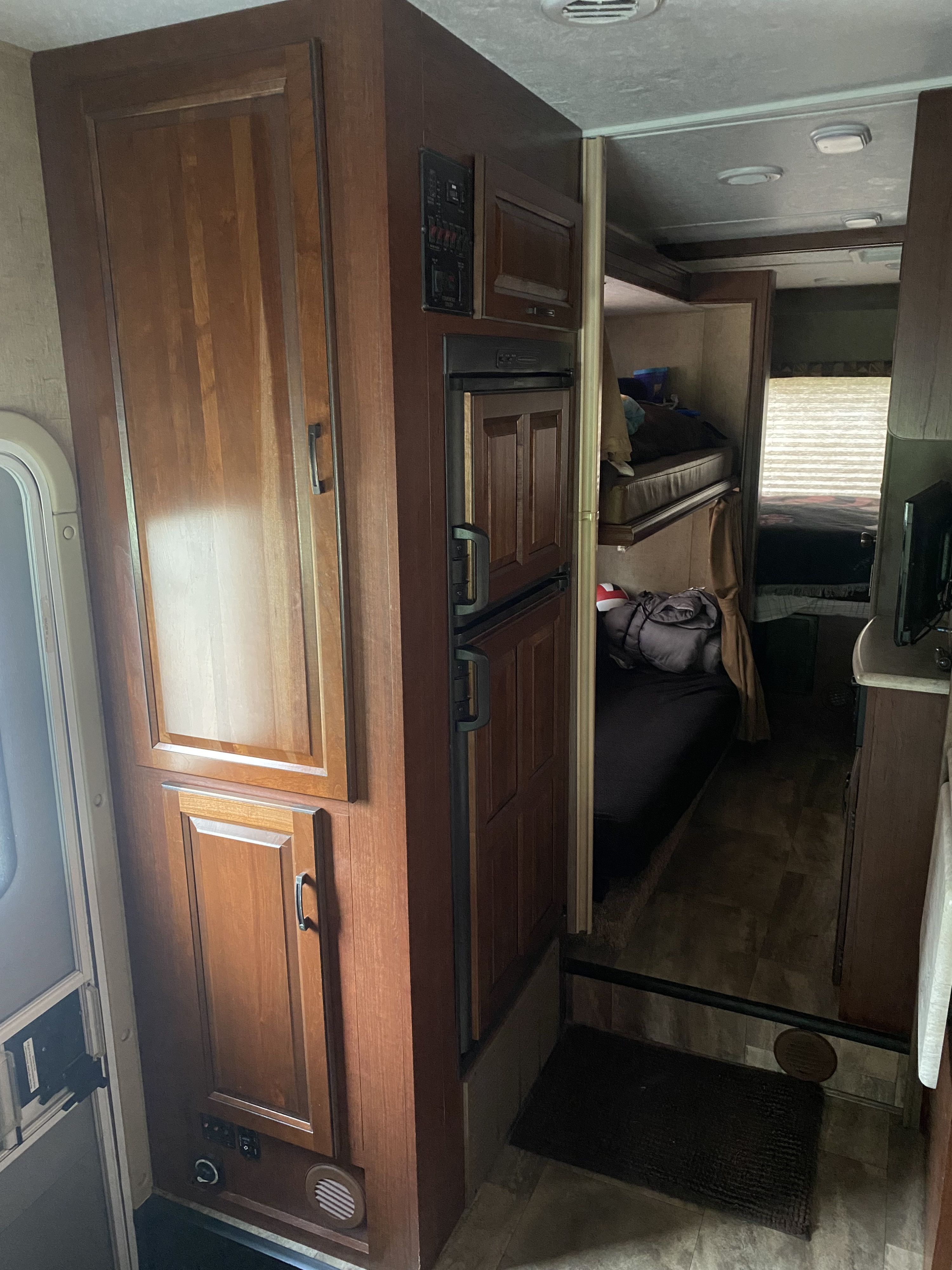 This RV rental interior features wooden cabinets, a refrigerator, and a control panel, with a view of cozy bunk beds beyond.. Forest River Sunseeker 2016