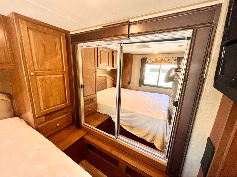 RV rental bedroom with spacious mirrored closet, comfortable bed, and wooden cabinetry for storage.. Coachmen Leprechaun 2017