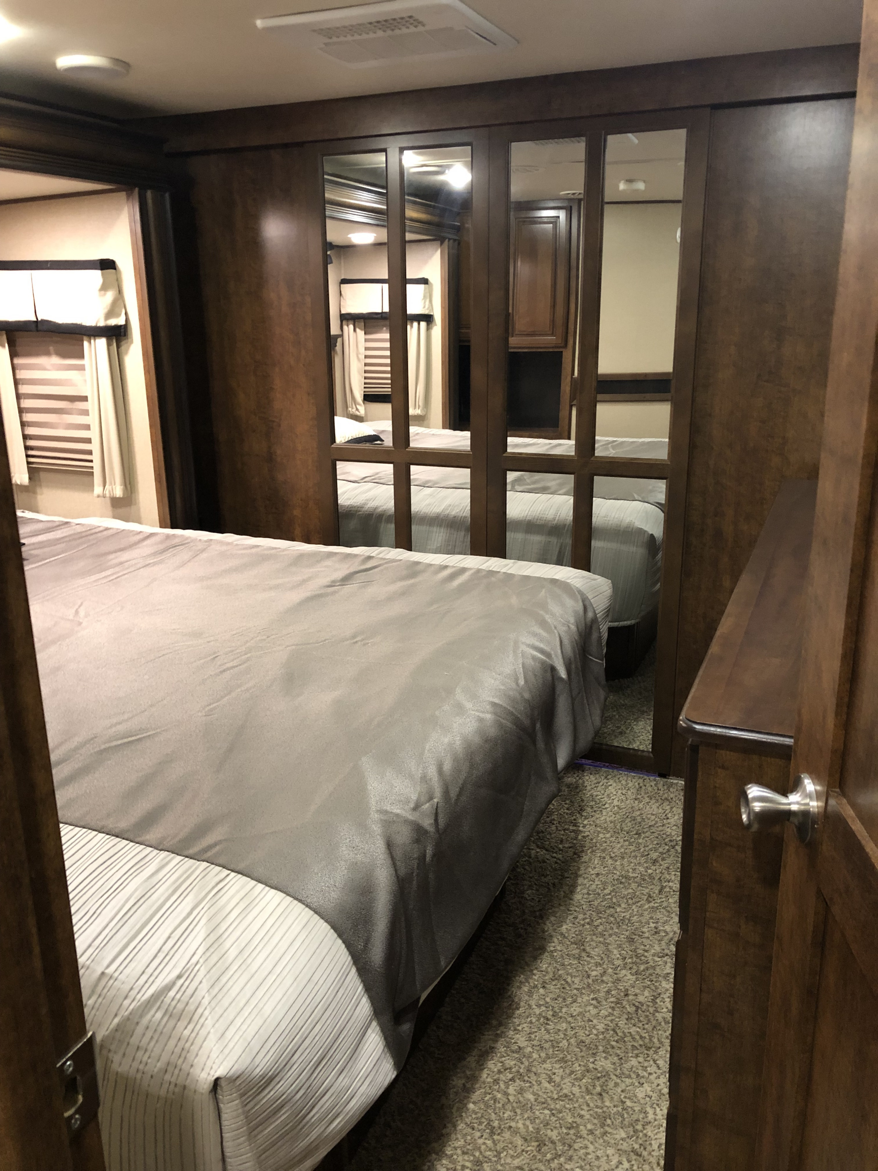 Interior of an RV rental bedroom: large bed, brown wood cabinetry, mirrored wardrobe, and soft carpet.. Grand Design Solitude 2015