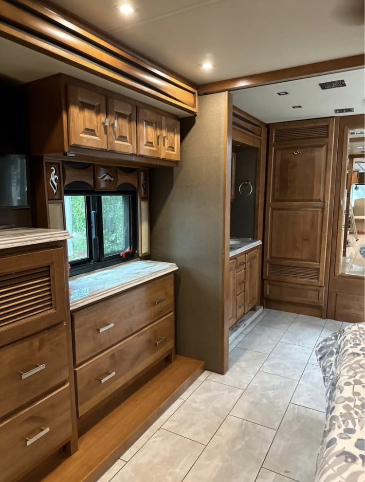 Luxury RV rental bedroom suite featuring wood cabinets, dresser, tiled floor, and a connecting private vanity area.. Tiffin Motorhomes Phaeton 2019