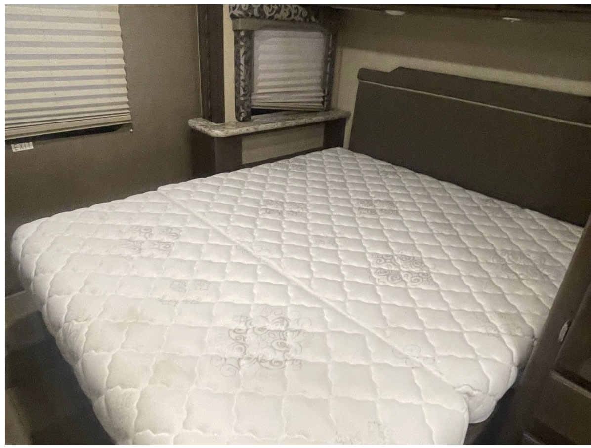 The inviting bedroom of an rv rental, with a clean white mattress, headboard, and window blinds. An "EXIT" sign is visible.. Thor Four Winds 2017
