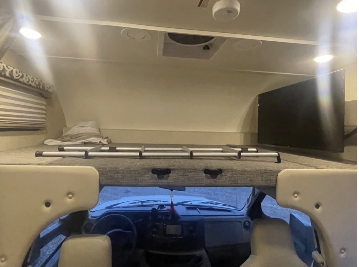 RV rental's spacious cab-over bunk, featuring a cozy bed with a ladder and a mounted TV for entertainment.. Thor Four Winds 2017