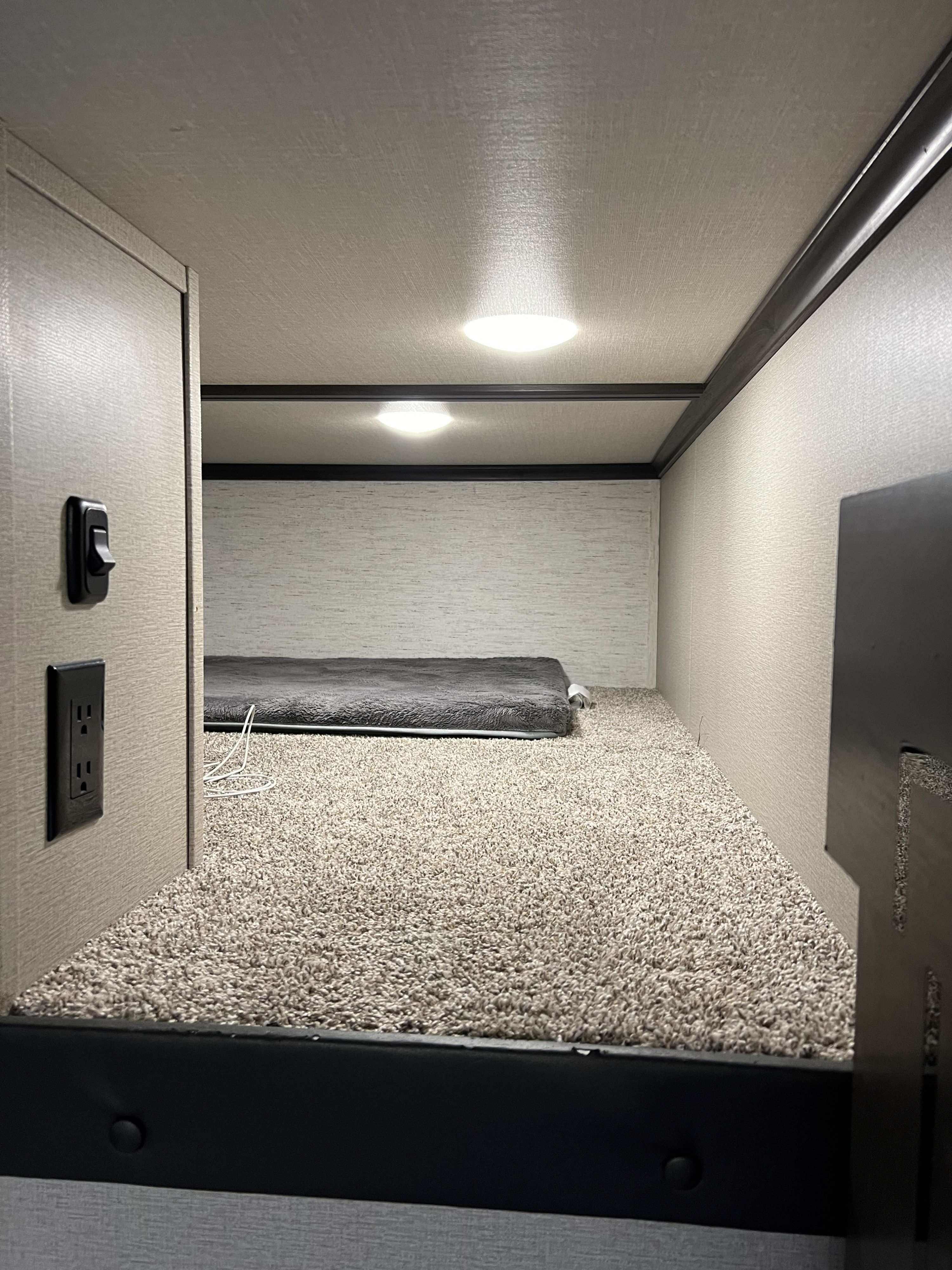 Inside an RV rental, a carpeted upper bunk sleeping area is seen, with bright ceiling lights and a simple gray mattress.. Grand Design Momentum 2021