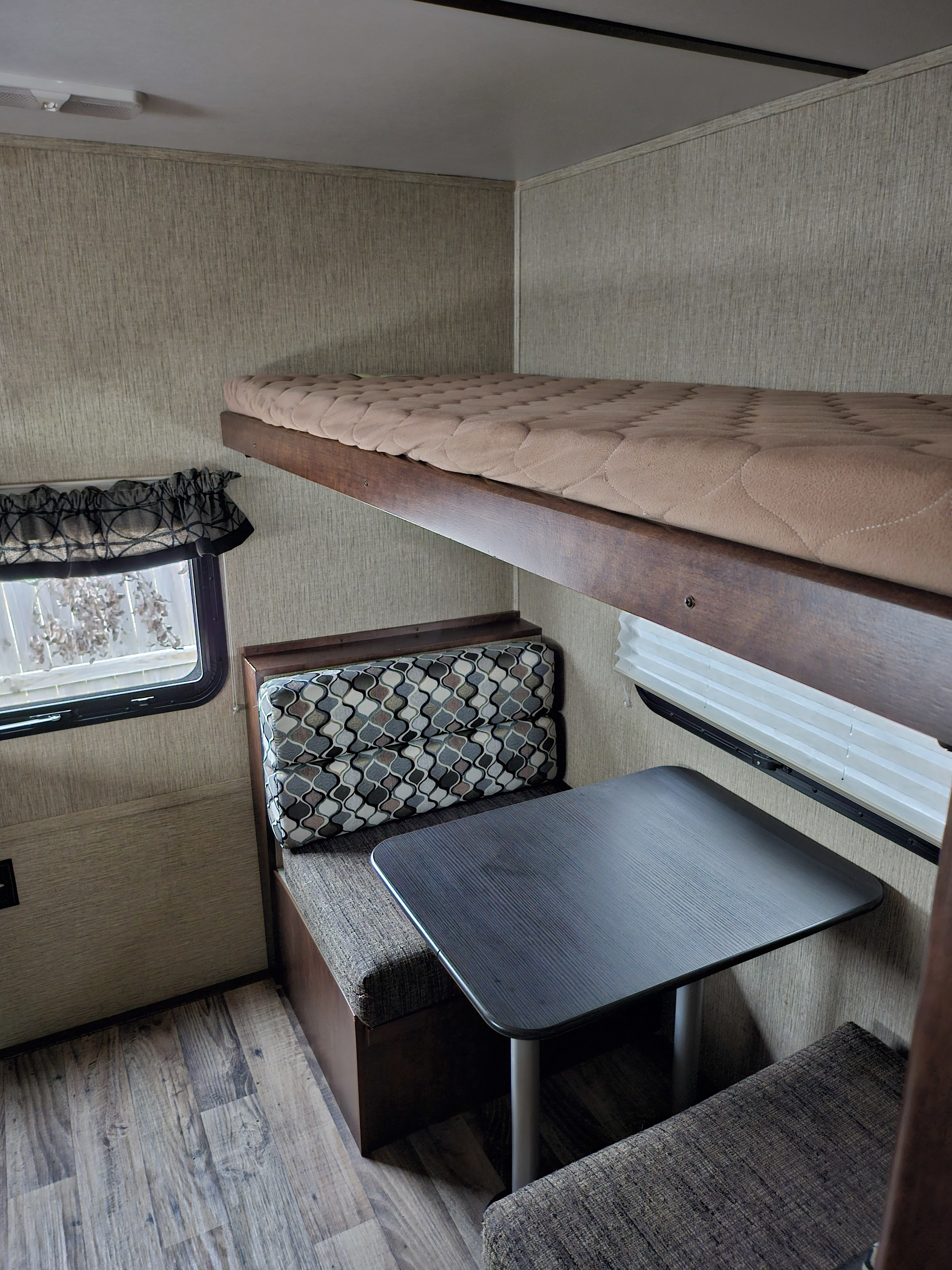 Cozy RV rental interior features comfortable bunk beds above a functional dinette with a dark table, all on wood-look flooring.. Keystone Outback 2018