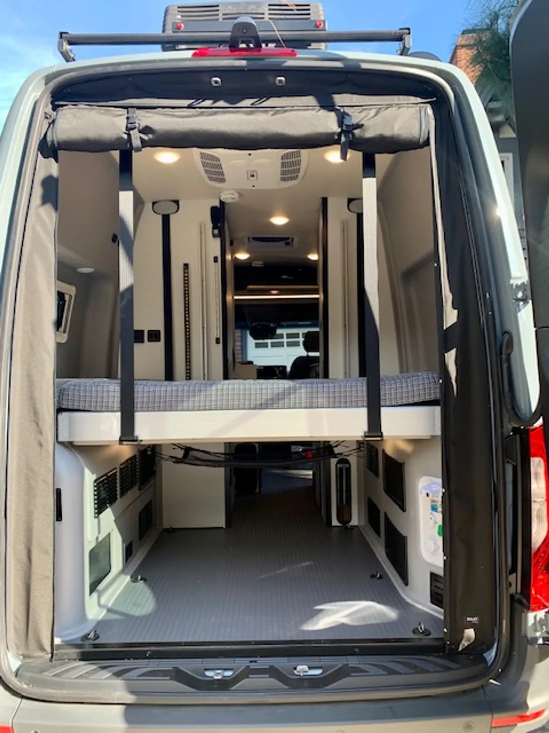 RV rental van interior from rear, showing a raised bed with spacious storage below. A clean, modern space for travel.. Winnebago Revel 2022