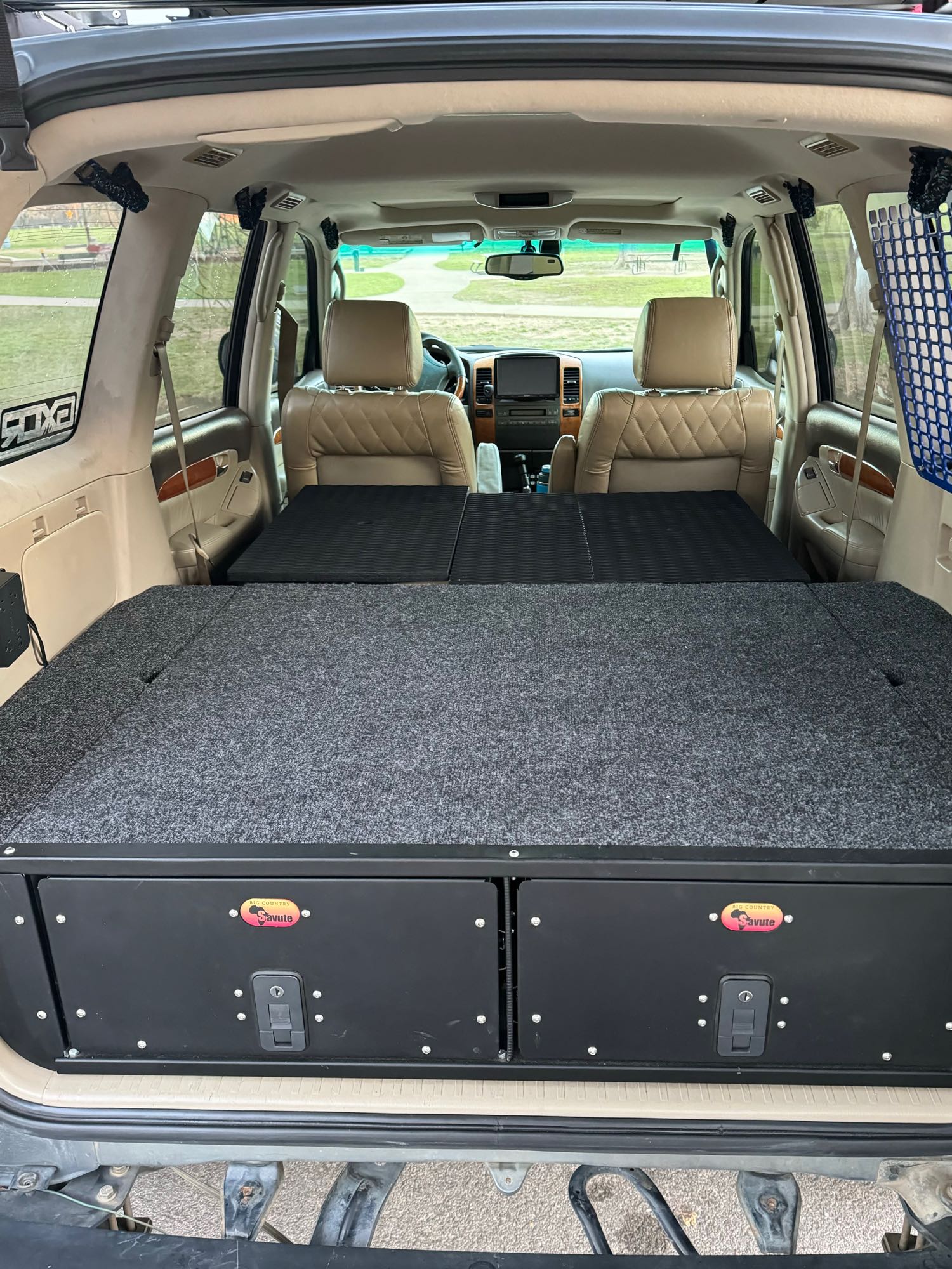 SUV's custom interior features a sleep platform and storage drawers, offering an RV rental experience for camping.. Lexus GX470 2003