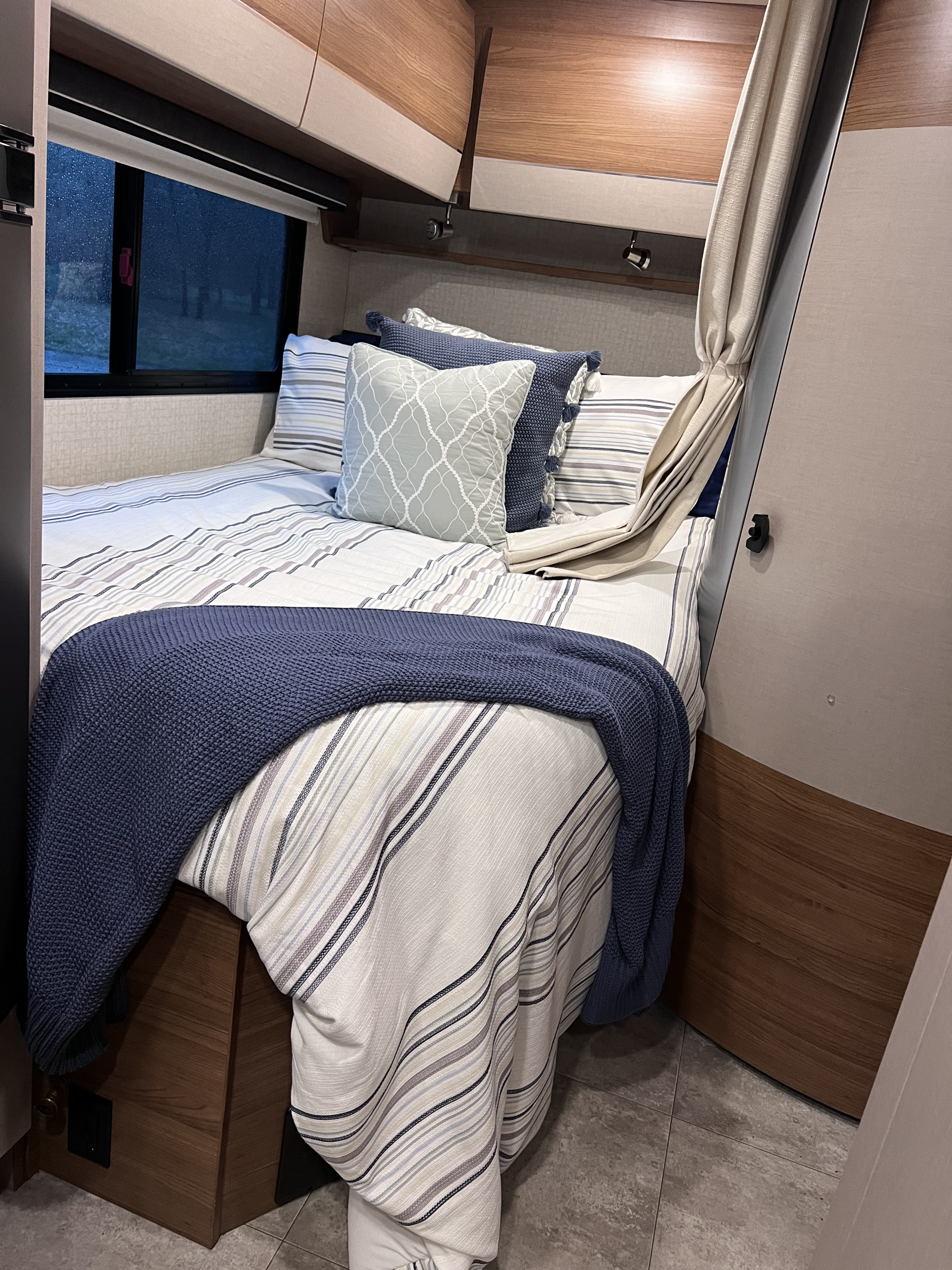 Cozy RV rental bedroom with striped bedding, blue throw, and overhead storage. Perfect for a comfortable travel stay.. Winnebago Mercedes Navion 2016