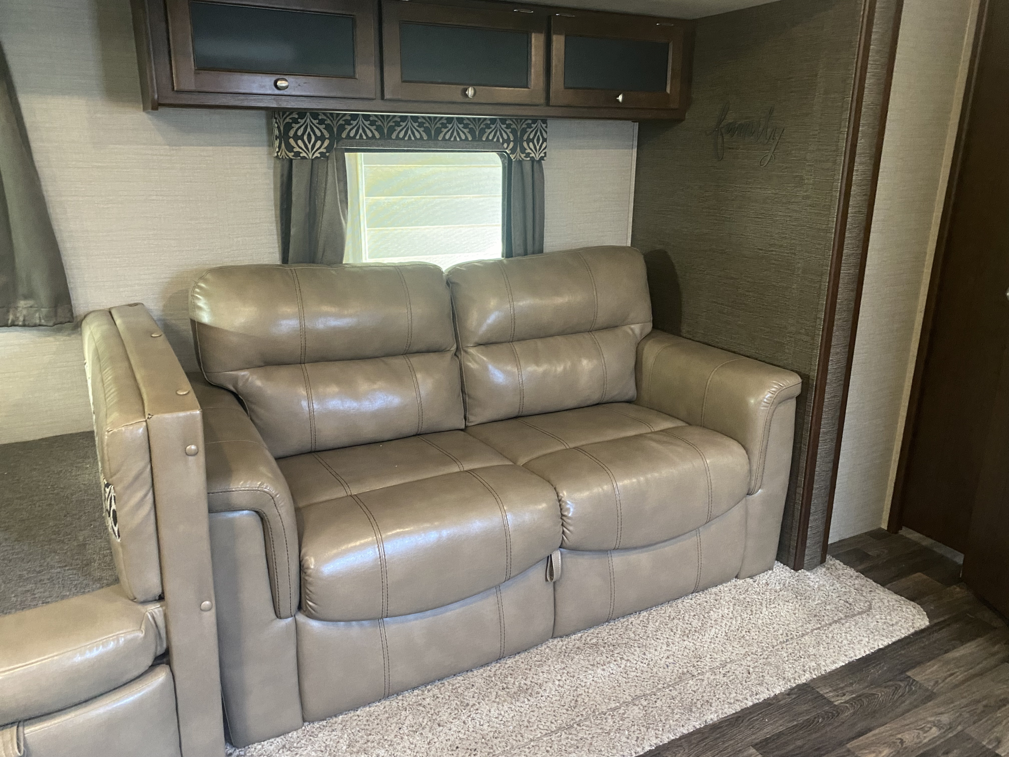 Cozy RV rental interior featuring a comfortable reclining sofa, overhead cabinets, and a window for natural light.. Keystone RV Bullet Premier 2017