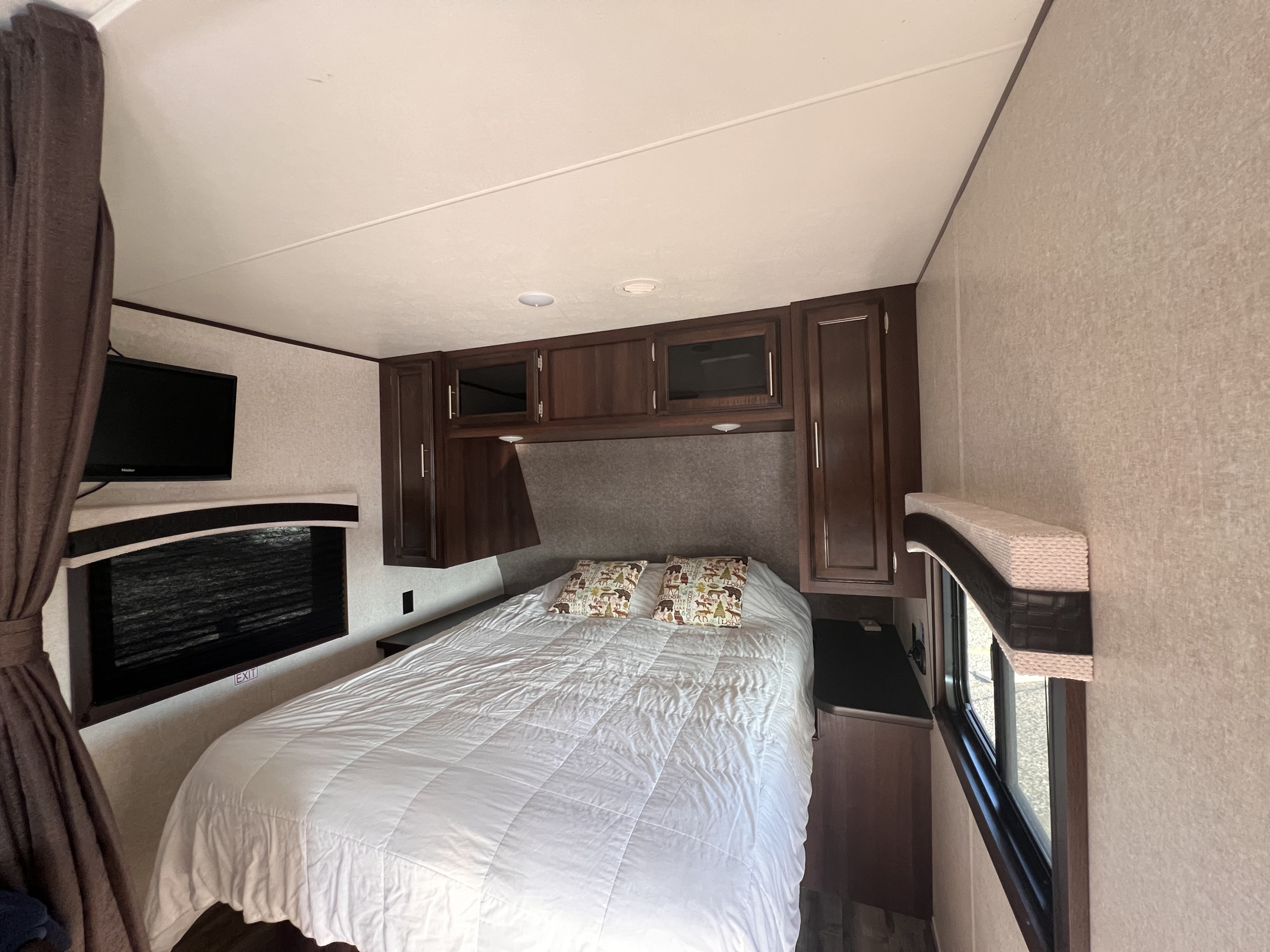 Inside an RV rental, a compact bedroom features a bed with white comforter, wood cabinets, and TV.. Jayco Jay Flight 2019