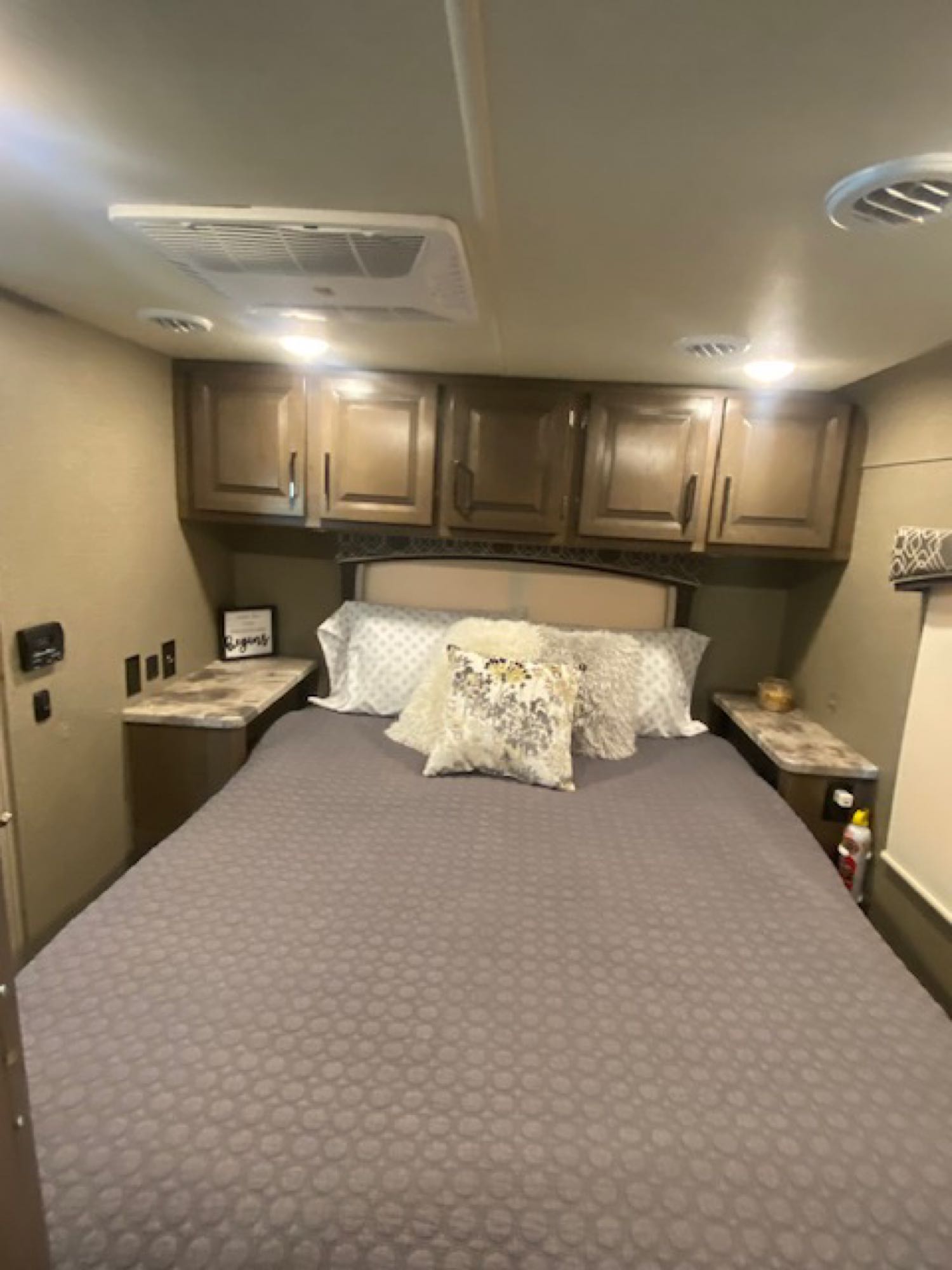 This cozy RV rental bedroom features a comfortable bed, overhead cabinets, bedside tables, and a ceiling-mounted AC unit.. Thor Chateau 2021