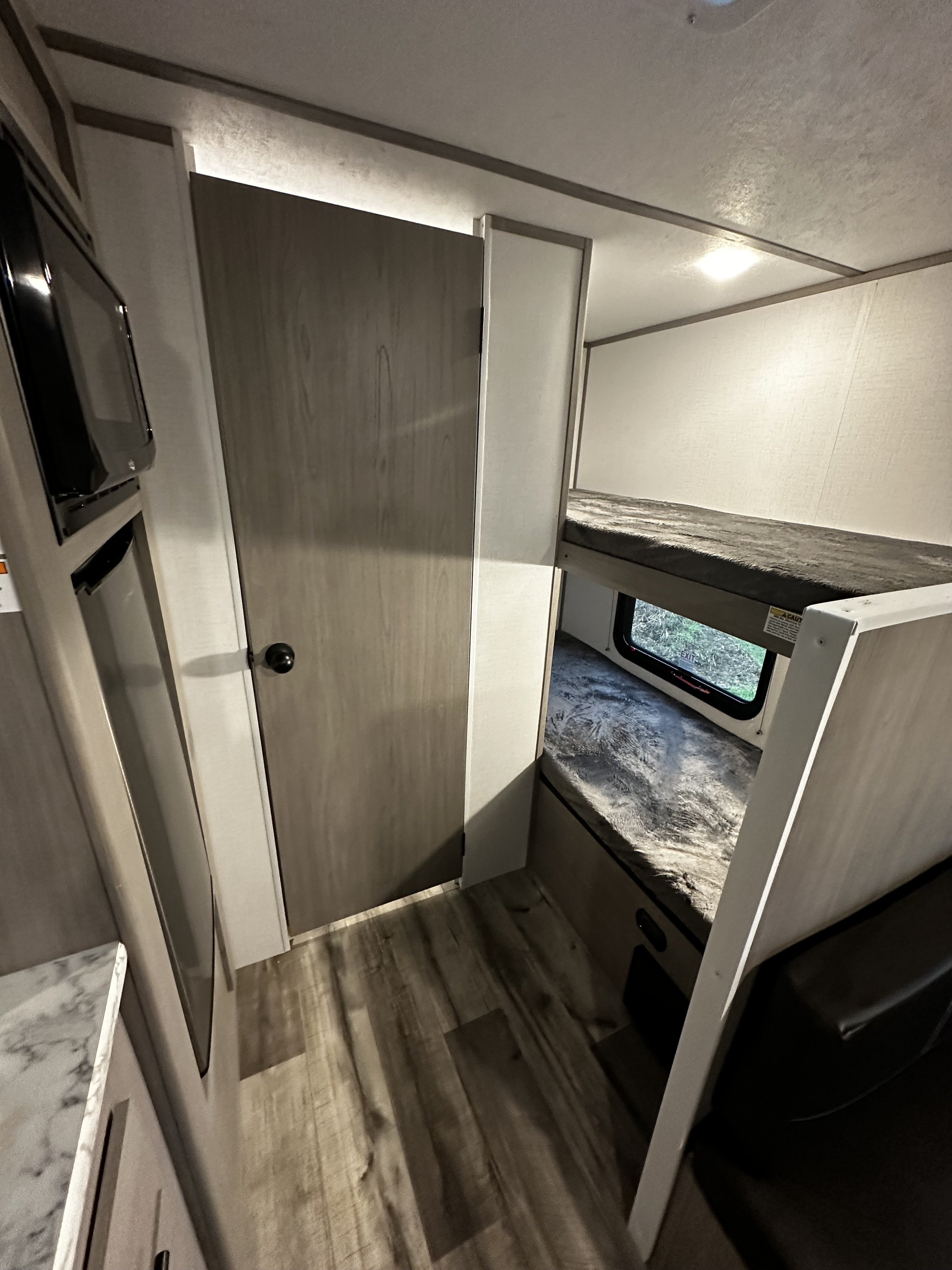 Compact RV rental interior featuring bunk beds for sleeping, a microwave, and a door, designed for efficient use of space.. Other 17 B 2024