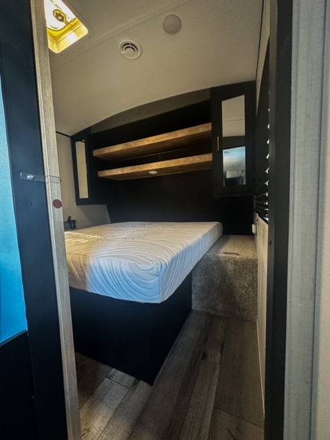 RV rental bedroom interior: Features a comfortable white mattress, wooden shelves, and overhead storage.. Keystone RV Springdale 2022
