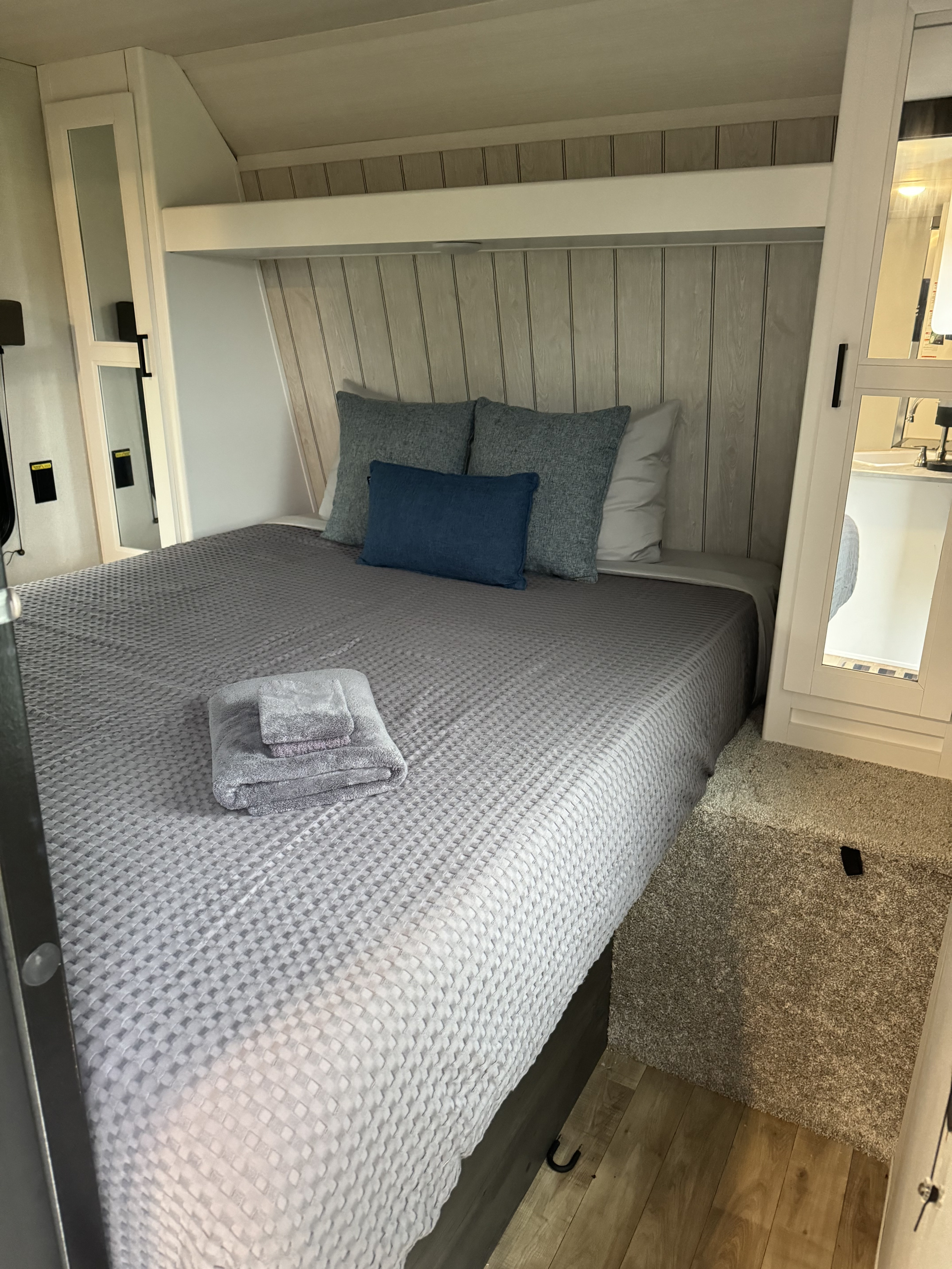 Experience comfort in this RV rental's bedroom, featuring a grey bed with soft pillows, towels, and built-in storage.. Keystone RV Hideout 2022
