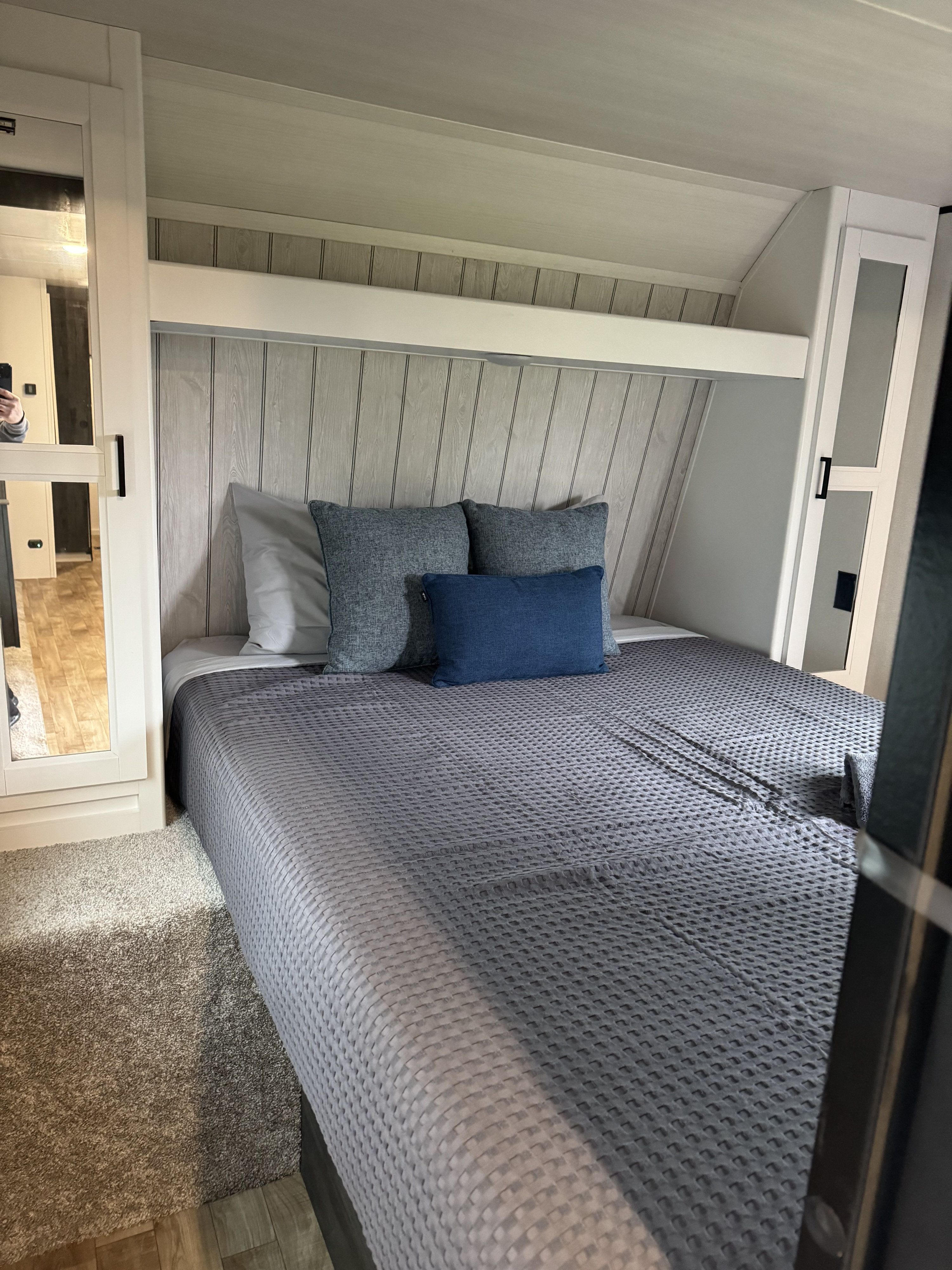Cozy RV rental bedroom with a grey waffle-pattern bed, blue pillows, & modern built-in storage, including a mirrored closet.. Keystone RV Hideout 2022