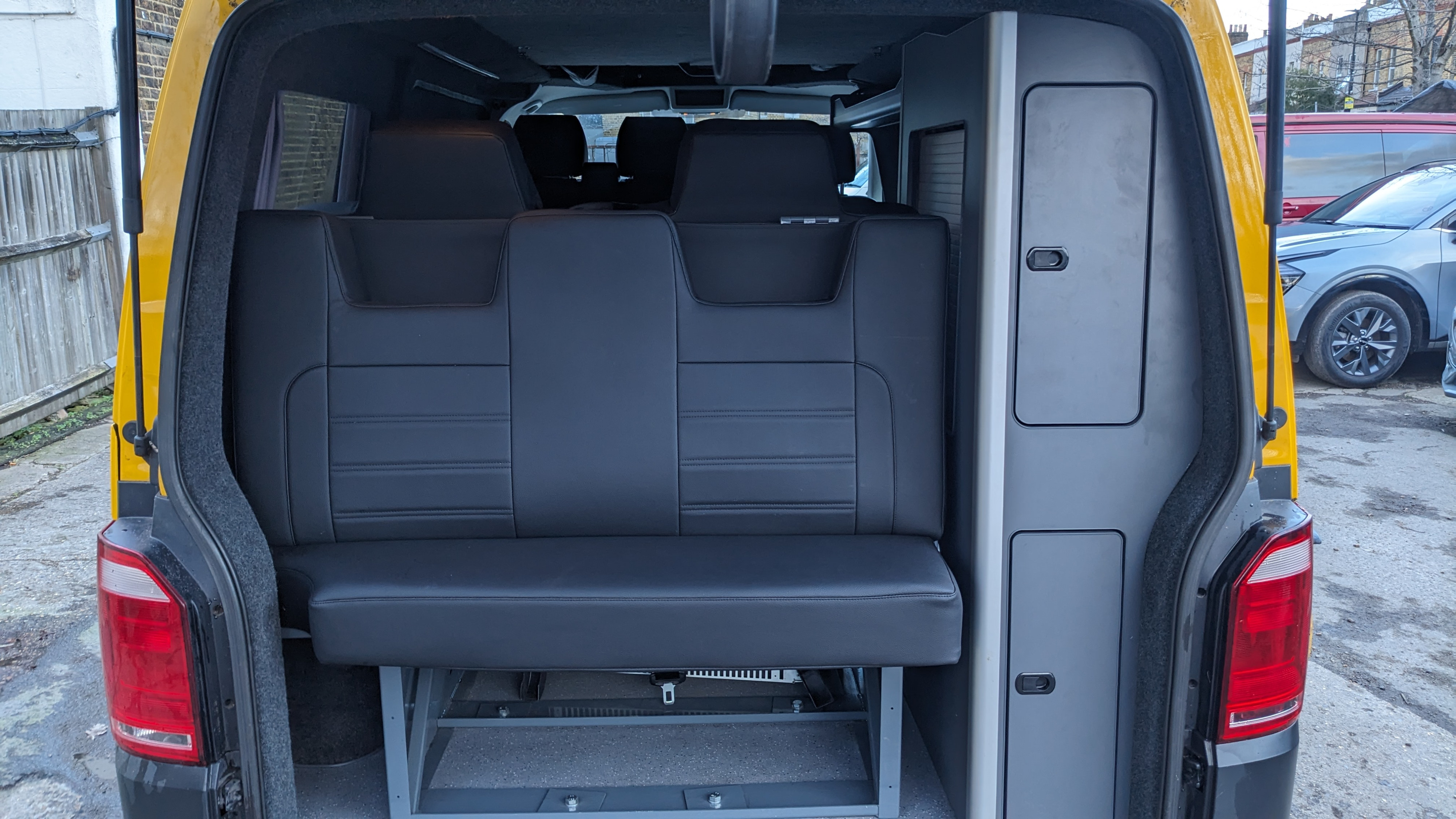 Rear view of a yellow campervan, ideal for RV rental. Features a black bench seat and built-in storage cabinets.. Volkswagen T6 2017