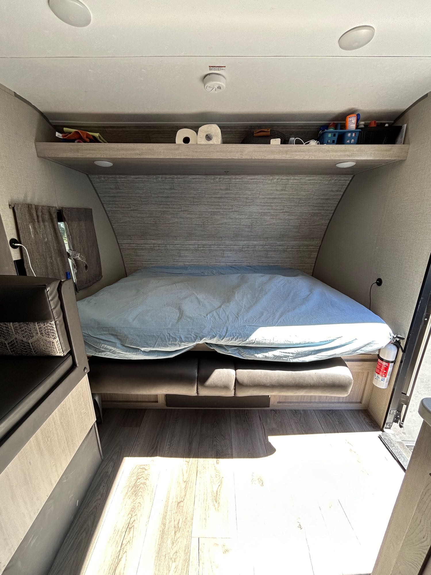 RV rental's sleeping area: a neatly made bed, overhead shelf with supplies, bench seating, and wood floor.. Coachmen 184BH 2023