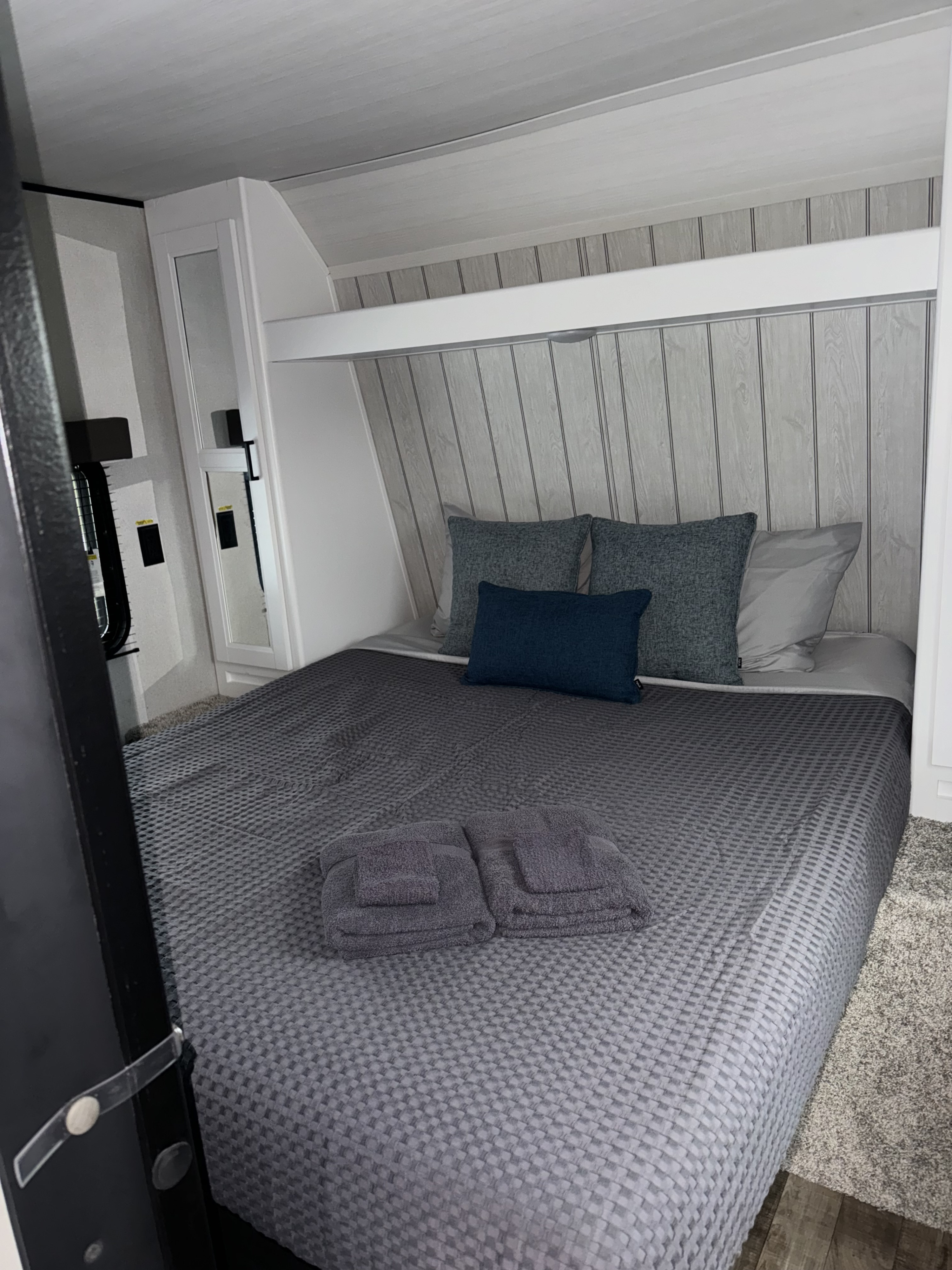 Cozy RV rental bedroom with a grey bed, blue pillows, and clean towels, featuring light wood paneling and compact storage.. Keystone Hideout 2022