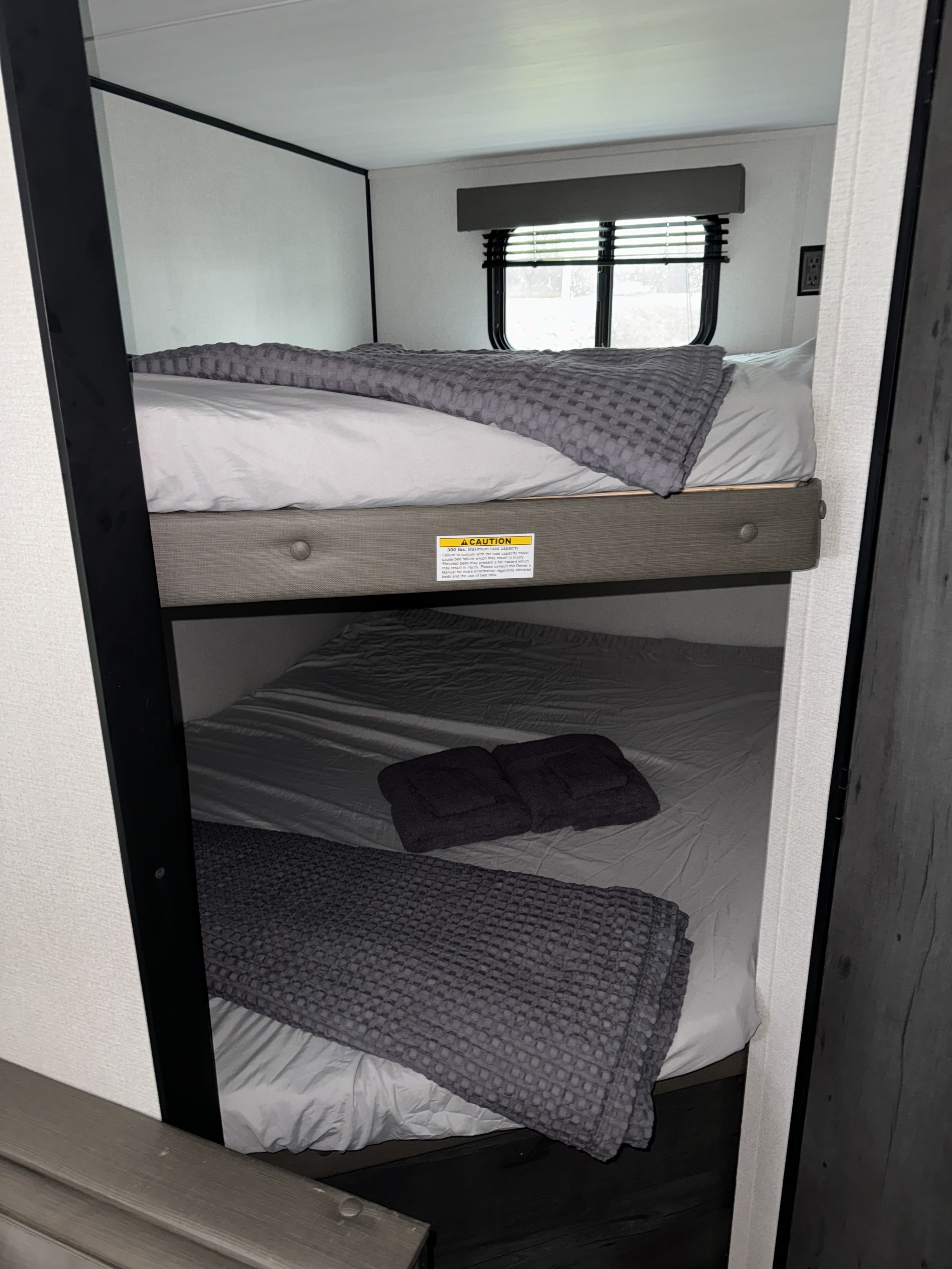 RV rental bunk beds: Two cozy sleeping areas with gray bedding. Top bunk has a 300 lbs capacity warning label.. Keystone Hideout 2022