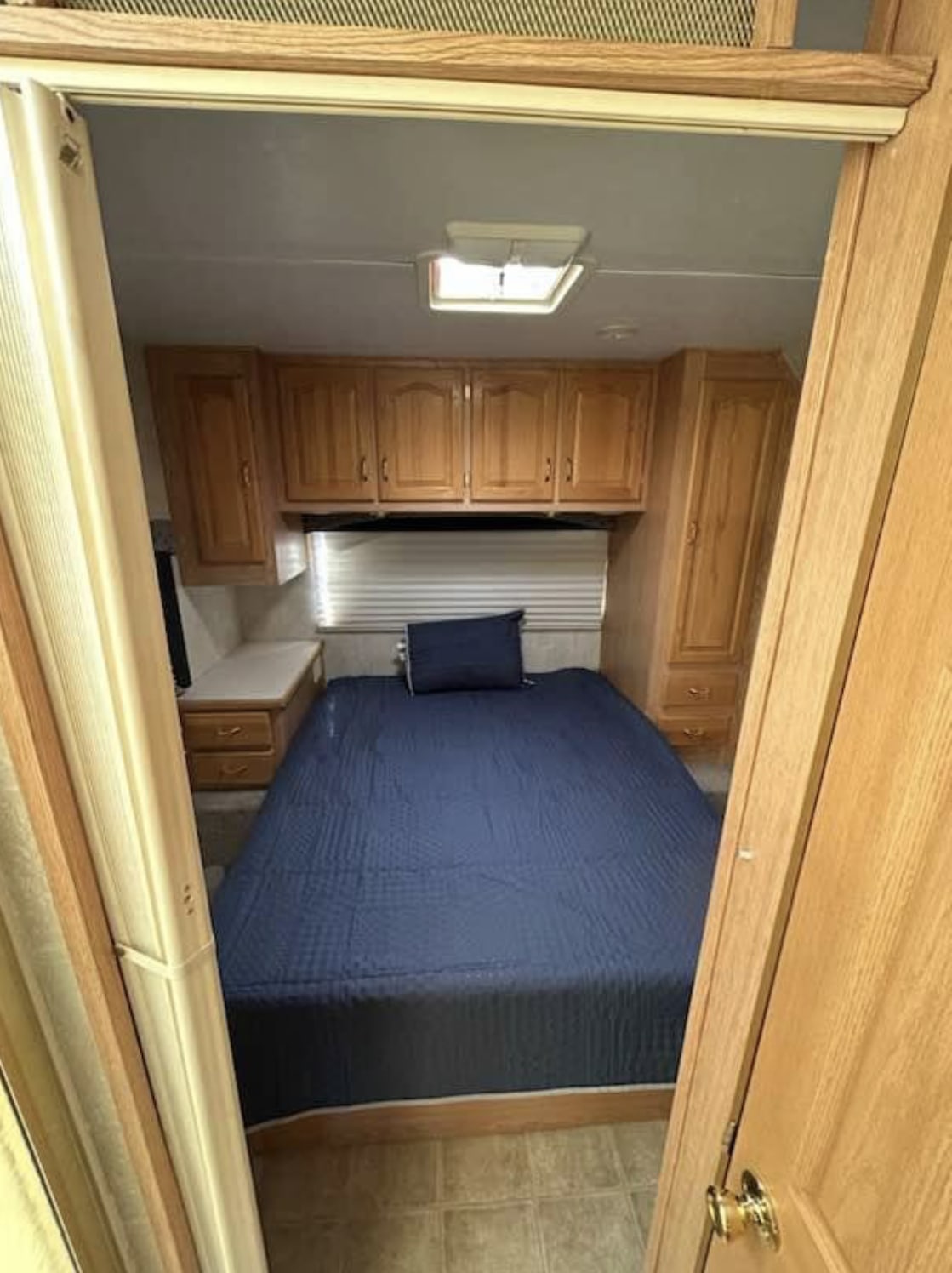 View into an RV rental bedroom with a blue quilted bed, light wood overhead cabinets, and built-in storage.. Forest River Sunseeker 2005