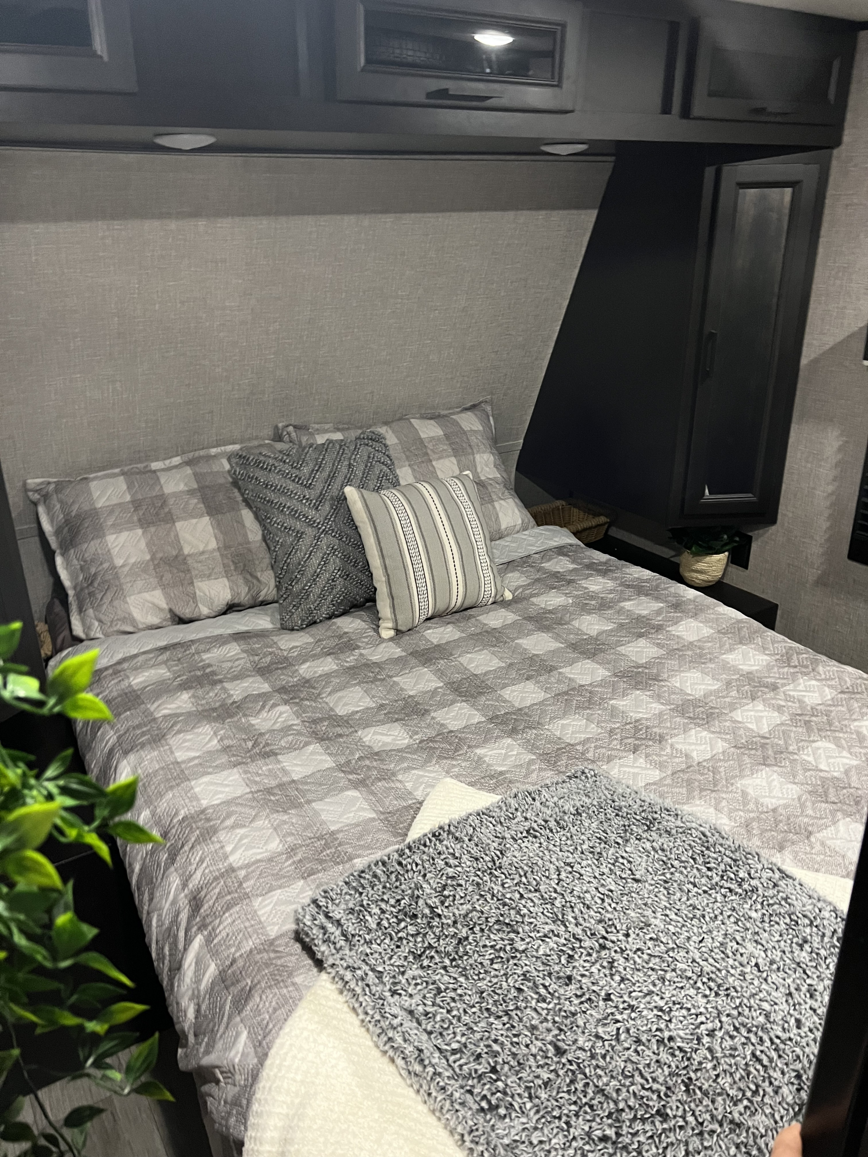 Cozy RV rental bedroom featuring a bed with gray plaid bedding, knit pillows, and overhead cabinets, designed for comfort.. Jayco Jay Flight 2022