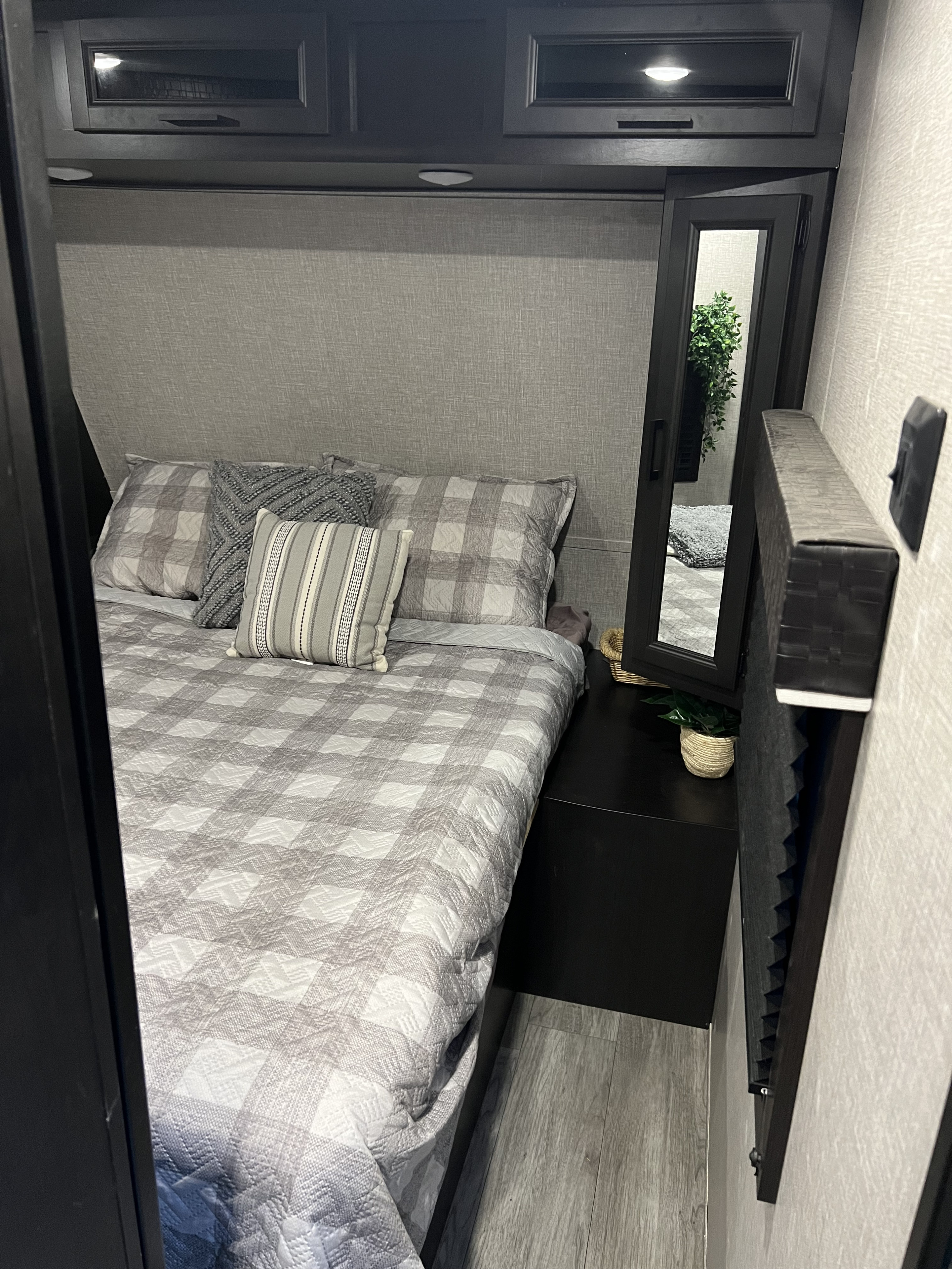 Plaid bedding, dark wood cabinets, and a mirrored nightstand create a cozy RV rental bedroom for comfortable travels.. Jayco Jay Flight 2022