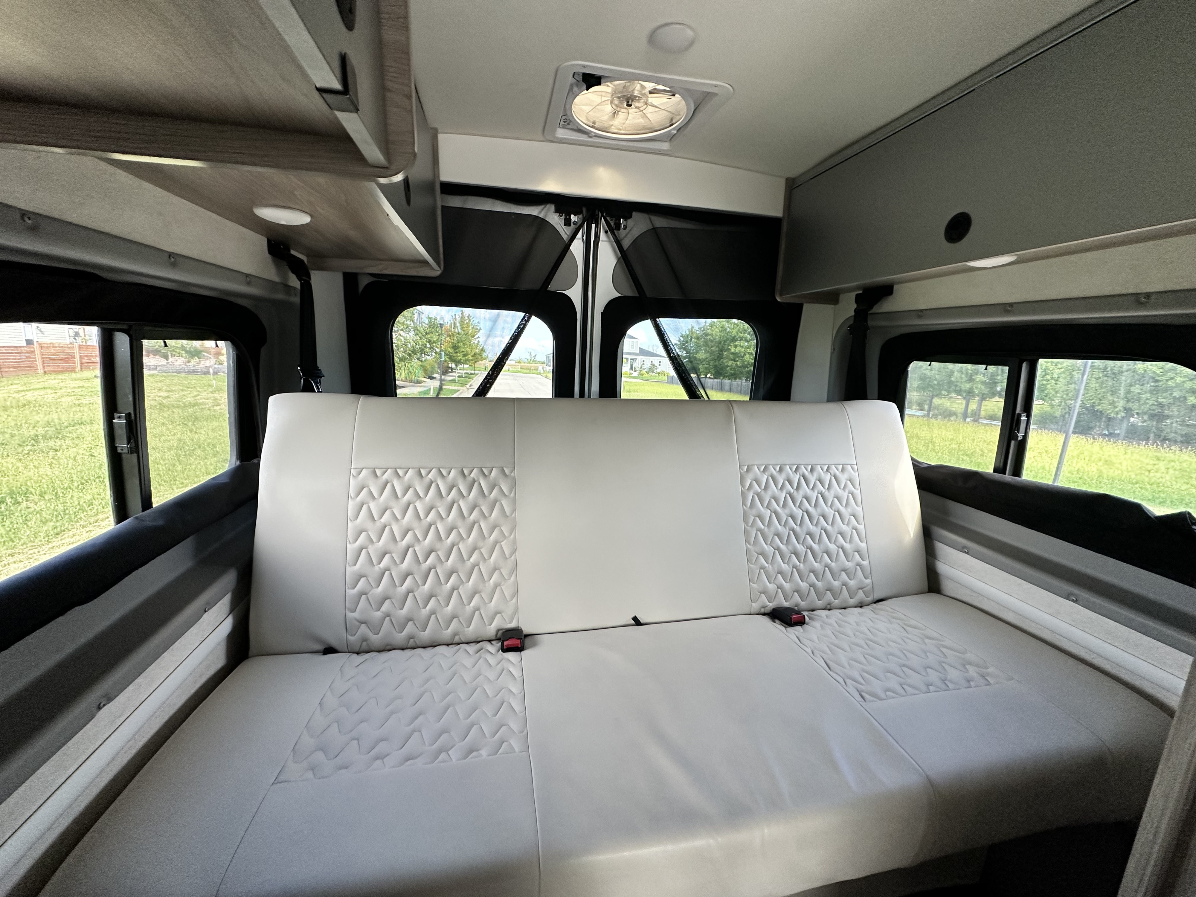 Modern RV rental interior with comfy white quilted bench seat/bed, overhead storage, and ceiling fan, ready for adventure.. Winnebago Solis 2021
