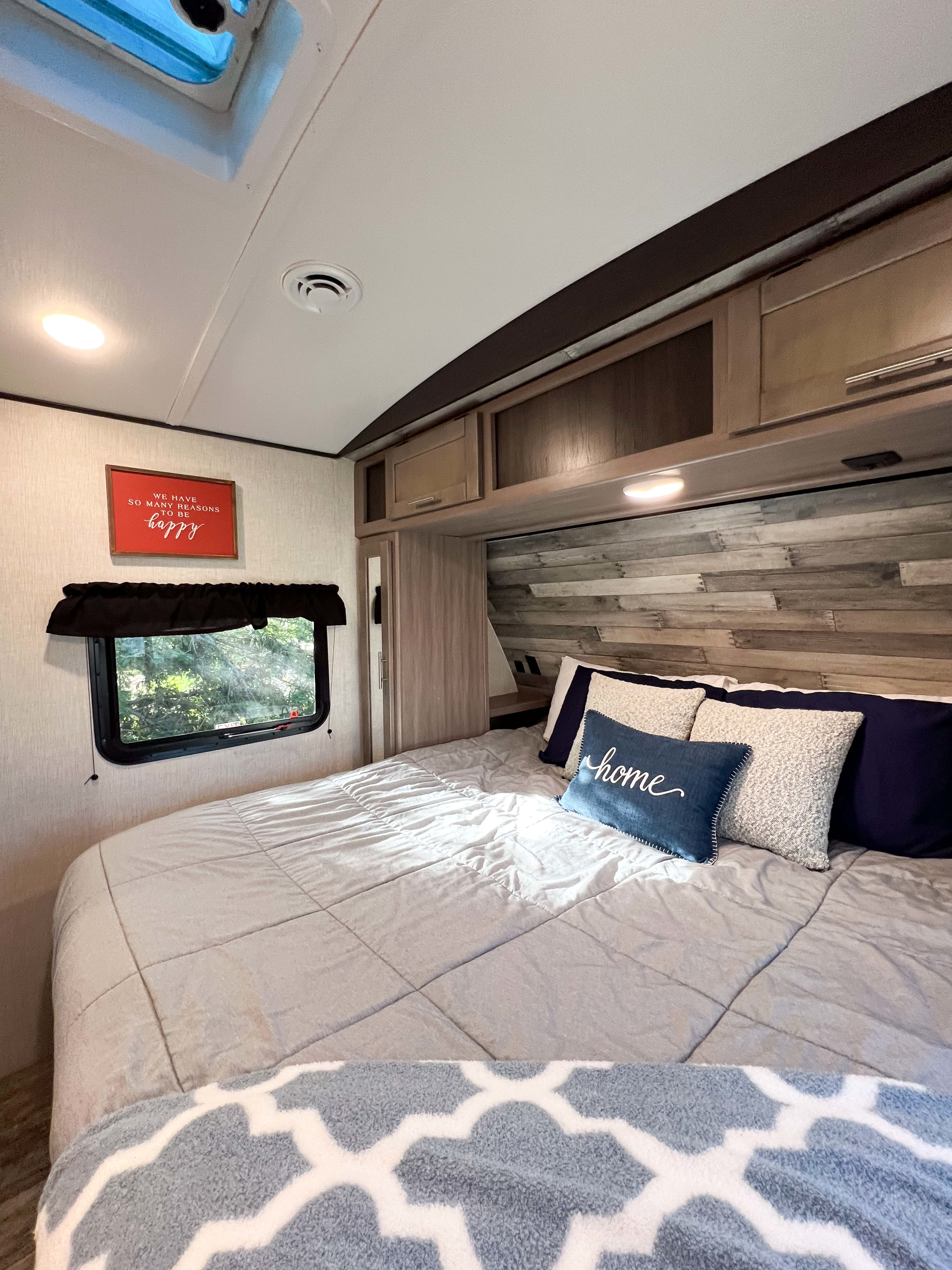 This cozy RV rental bedroom features a comfy bed, wood-paneled headboard, overhead storage, and natural light.. Crossroads RV Sunset Trail Super Lite 2022