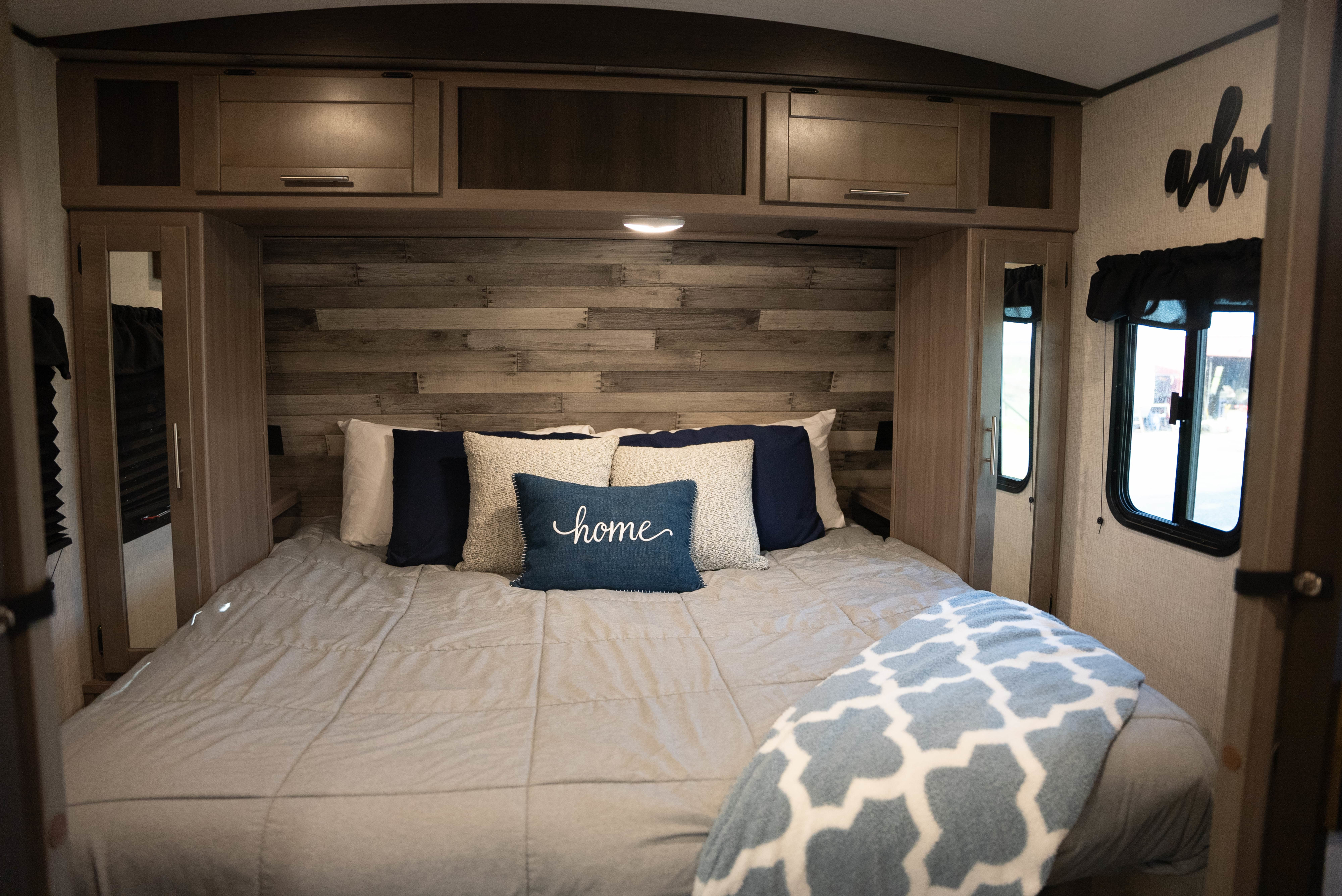 Cozy RV rental bedroom interior featuring a comfortable bed, wooden headboard, overhead cabinets, and a "home" pillow.. Crossroads RV Sunset Trail Super Lite 2022