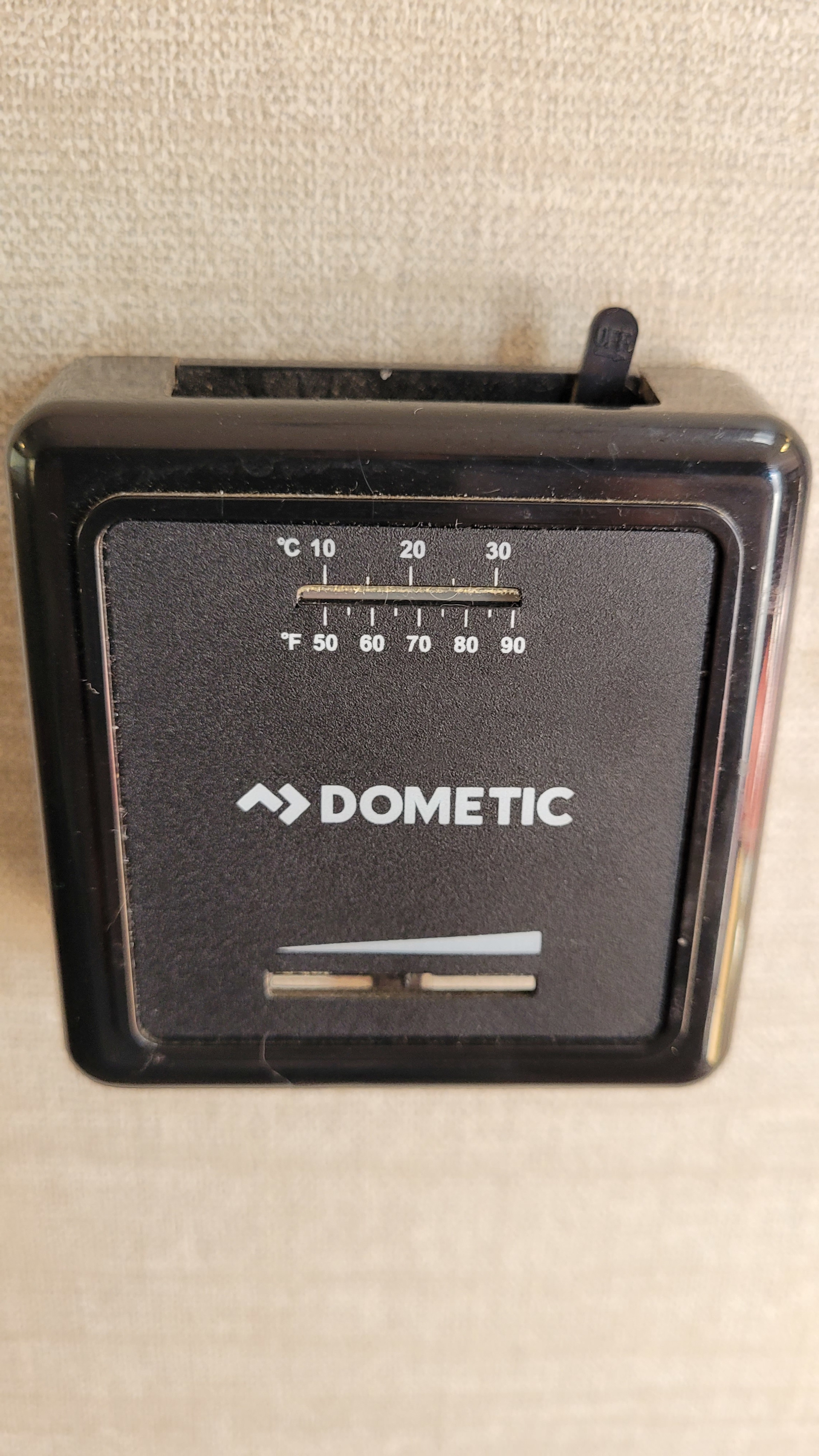 Black Dometic thermostat on wall, typical for RV rental, with C/F temp settings and an 'OFF' switch for climate control.. Keystone RV Bullet Crossfire 2019