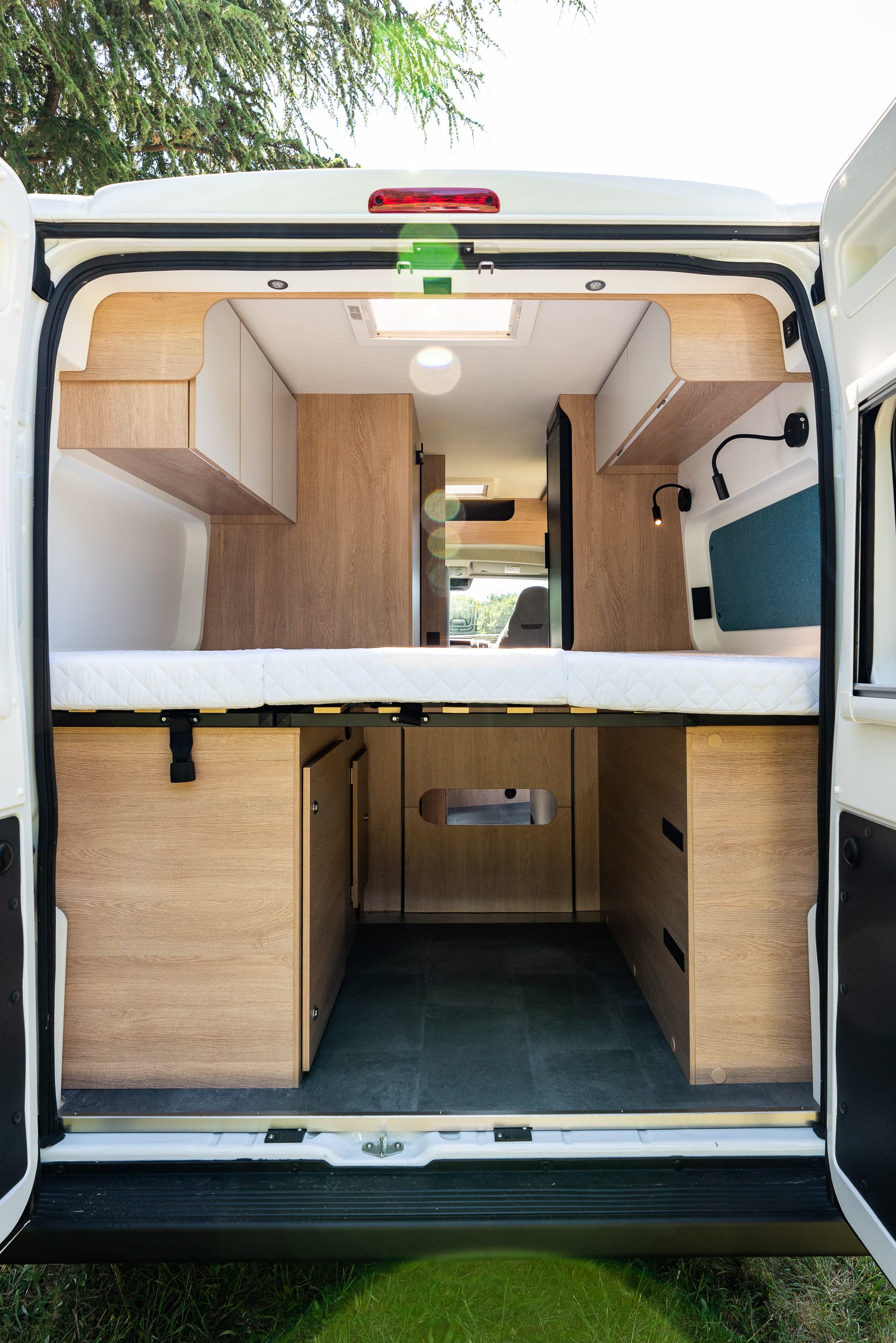 Inside a bright RV rental: a modern interior with a raised bed, under-bed storage, and sleek overhead cabinets.. joa 60G 2023
