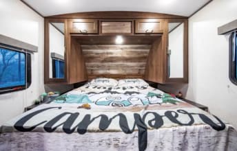 This comfortable RV rental bedroom features a wide bed with "CAMPER" bedding, wood paneling, and large windows.. Keystone RV Passport Grand Touring 2020