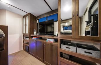 Explore this RV rental's cozy interior: a living space featuring a TV on wooden cabinetry with integrated storage.. Keystone RV Passport Grand Touring 2020