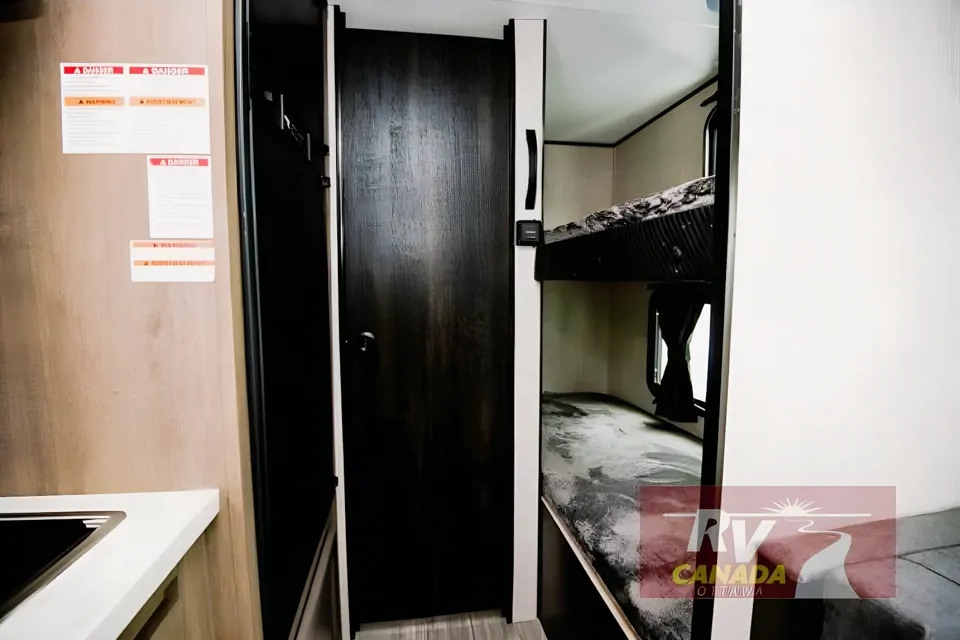 Inside an RV rental, this view shows comfortable bunk beds for guests in a travel trailer, with warning labels on the left.. Jayco Jay Flight SLX 2023