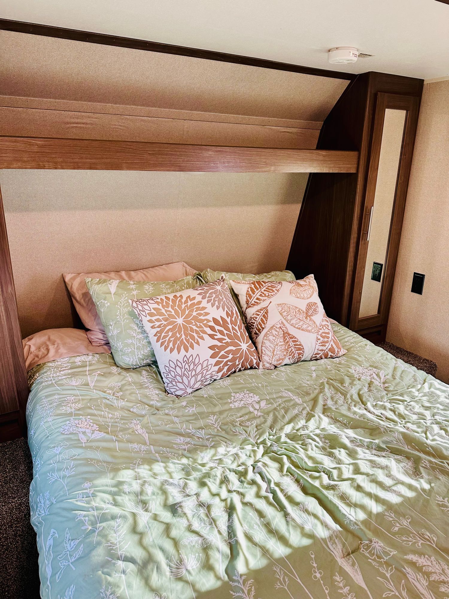 Inviting RV rental bedroom: green bed with botanical print, decorative pillows, overhead storage, and wardrobe.. Keystone RV Hideout LHS 2020