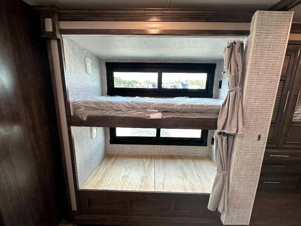 RV rental featuring built-in bunk beds with windows. Top bunk has a covered mattress, bottom is a wooden sleeping platform.. Entegra Coach Vision XL 2024