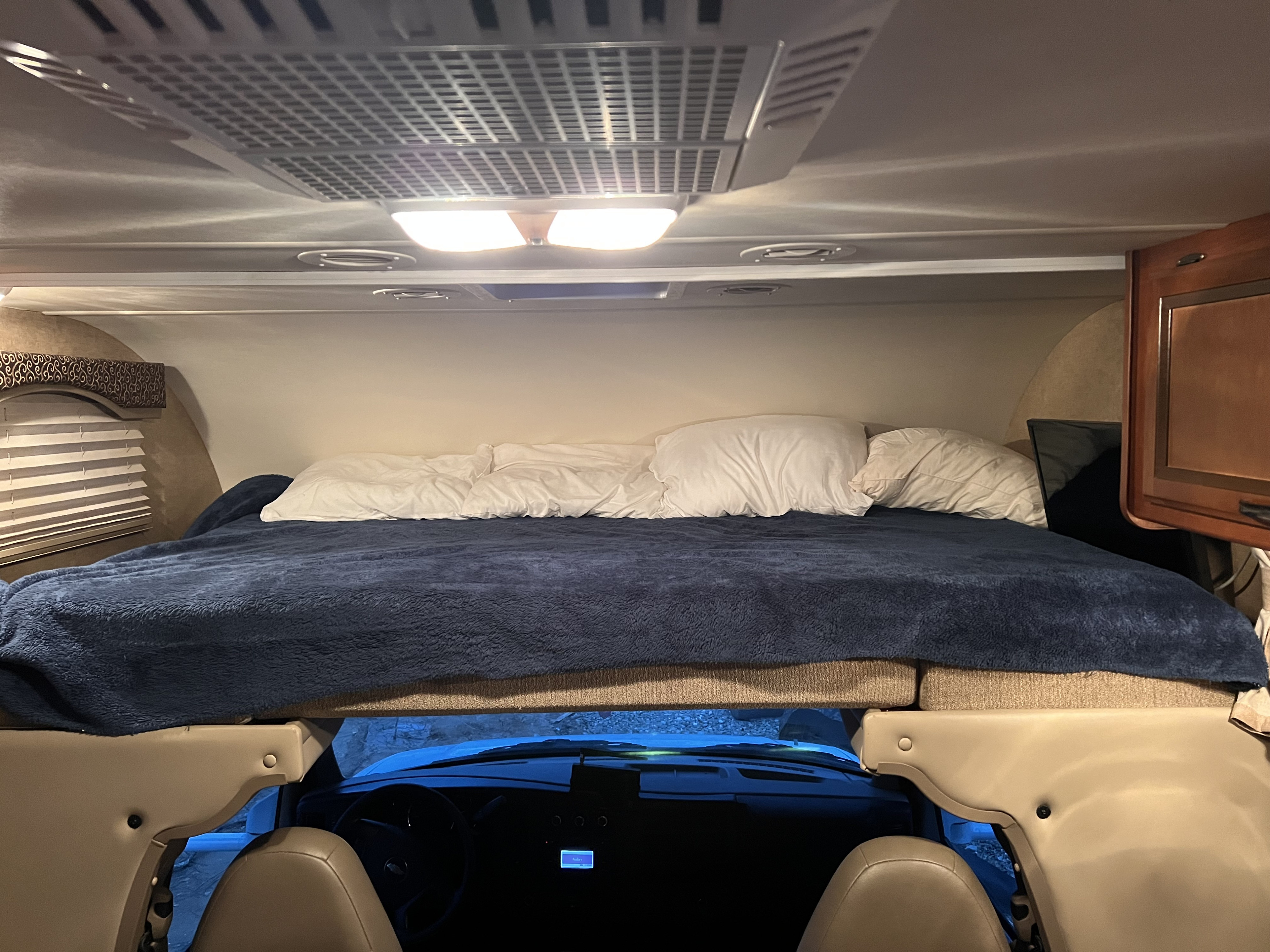 RV rental's cab-over bunk: a cozy bed with pillows & blue blanket, overlooking the vehicle's cockpit.. Thor Freedom Elite 2014